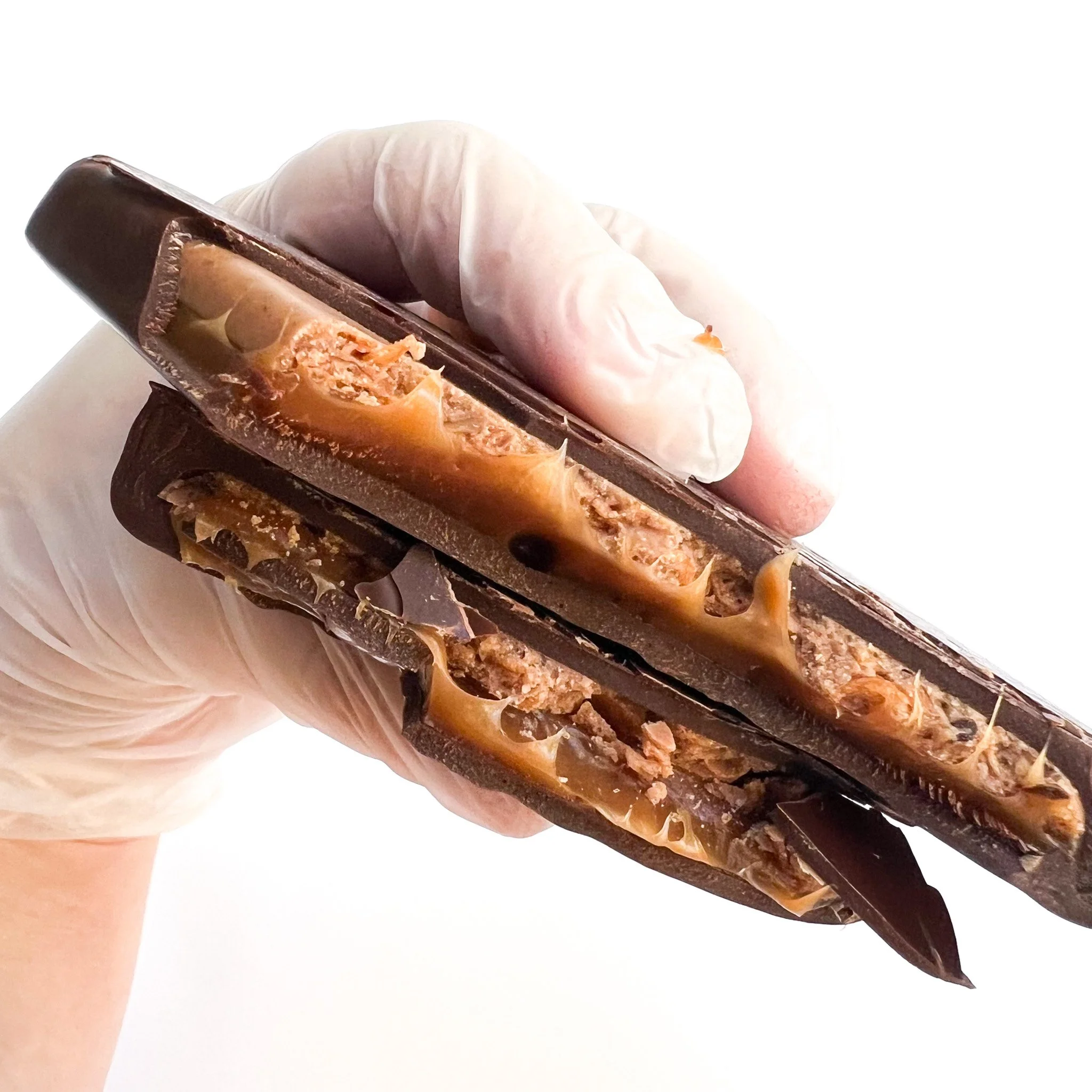 Person wearing gloves holding a chocolate-covered caramel candy bar.