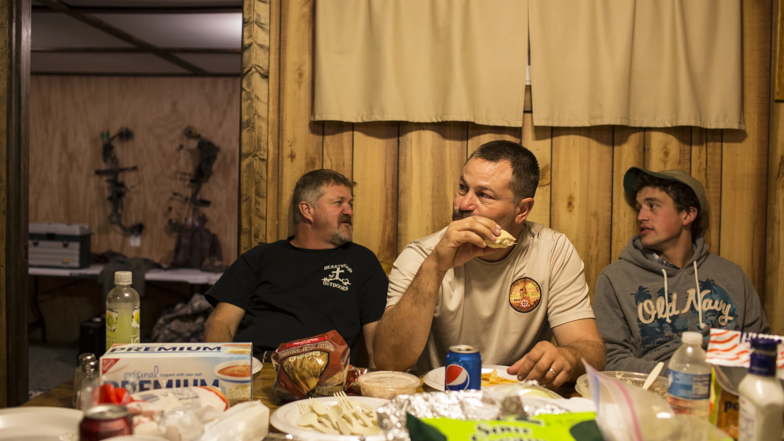 Tracy (L), his older brother Troy (C), and another hunter enjoy a evening meal after a hunt at the Heartwood Outdoors camp near Indian Springs, Maryland. 