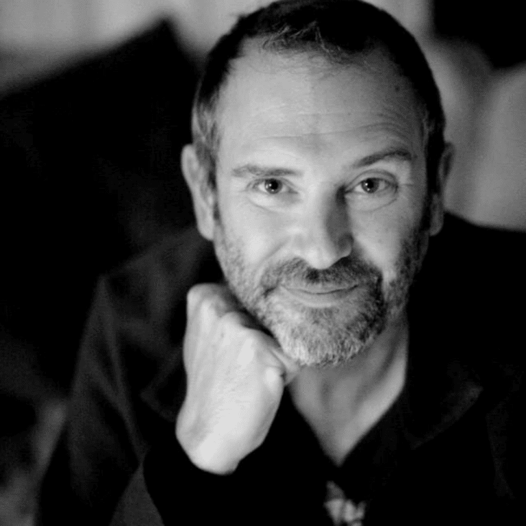 Close-up black and white portrait of a man with short hair, a beard, and a slight smile, resting his chin on his hand.