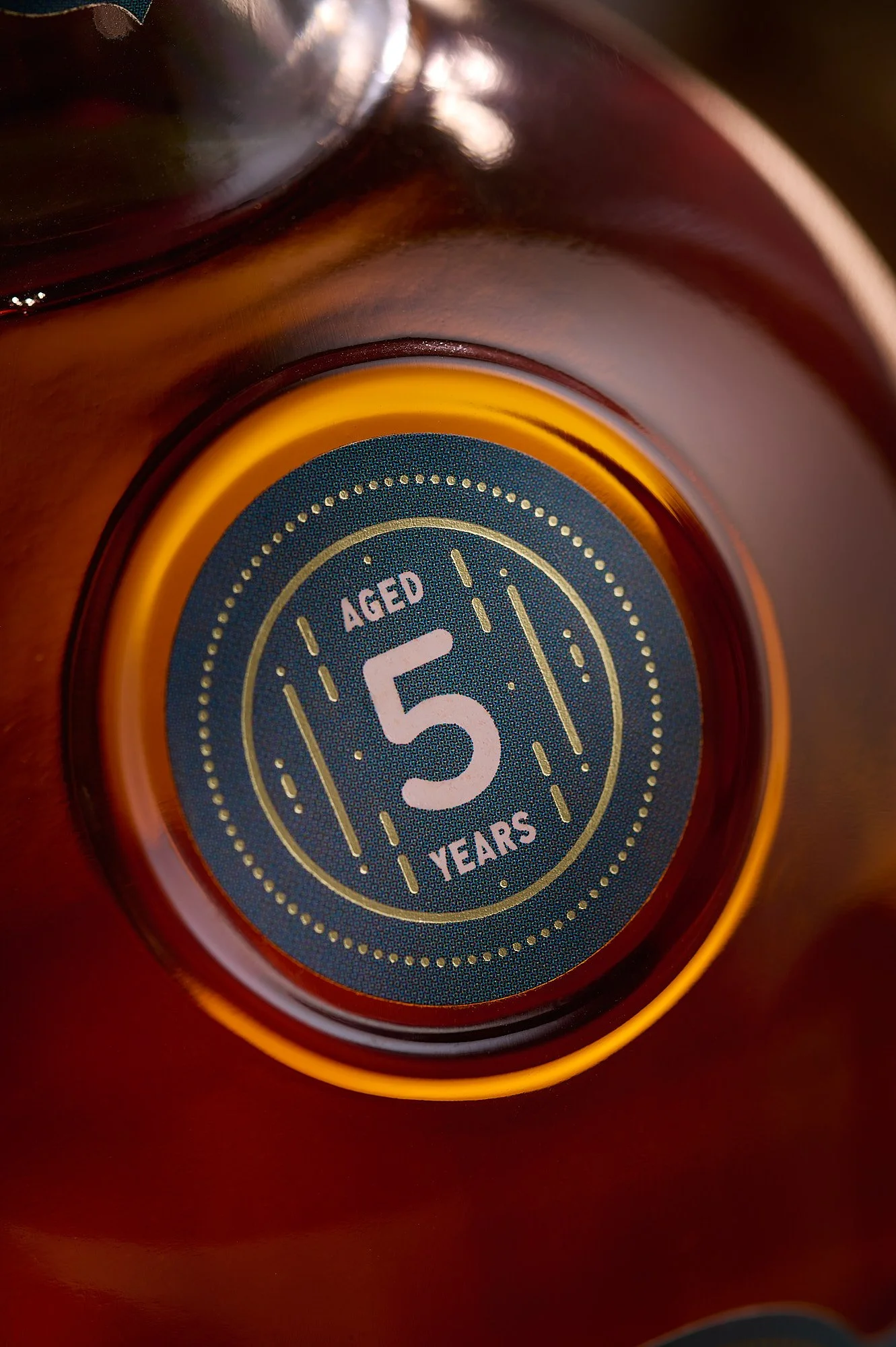 Spirits advertising photography by Dhanraj Emanuel — close-up of Bacoo 5-year aged rum bottle base detail. Commercial beverage photographer for rum and spirits brands, available nationwide.