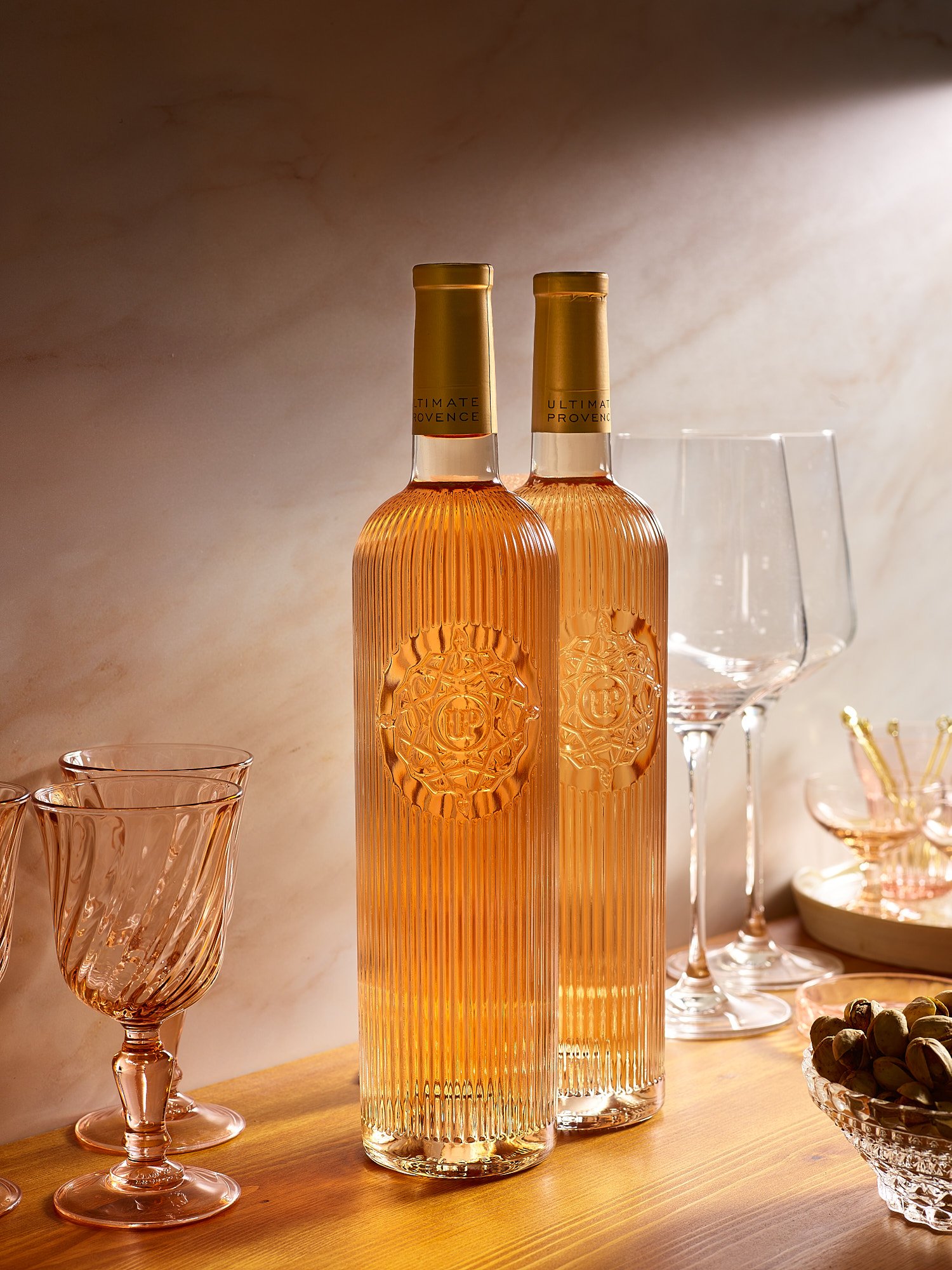 Commercial beverage photography by Dhanraj Emanuel — rosé wine bottles with gold caps, wine glasses, and pistachios on wooden surface. Spirits and beverage advertising photographer based in Greensboro NC, available nationwide.