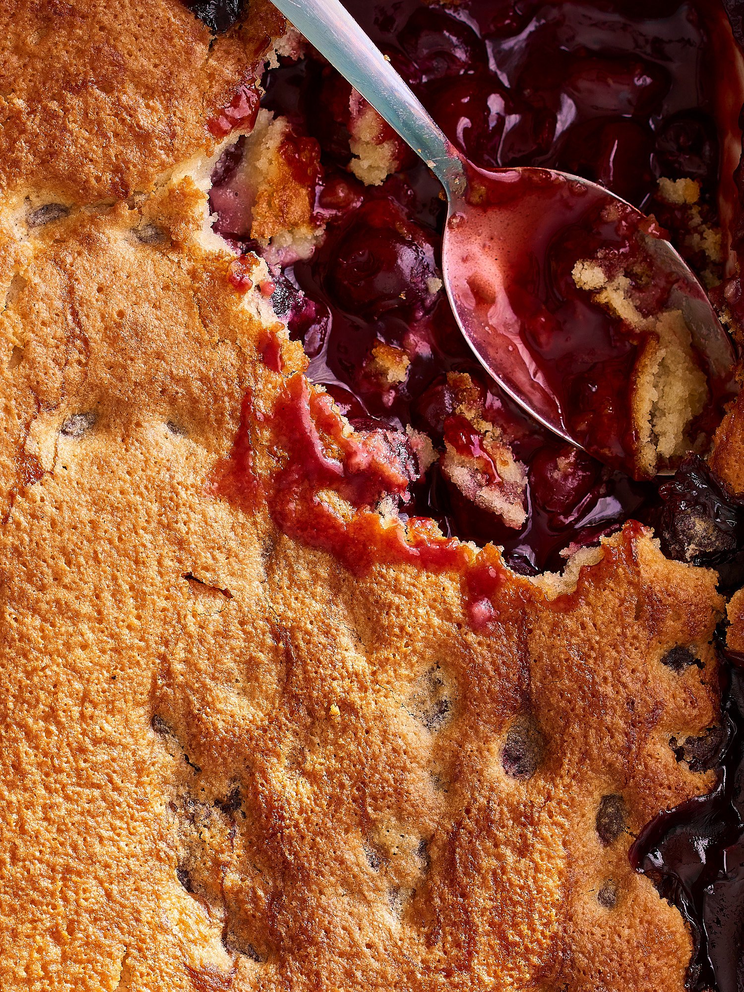 A close-up of a cherry cobbler with a golden, crumbly crust and cherry filling revealed on one side.