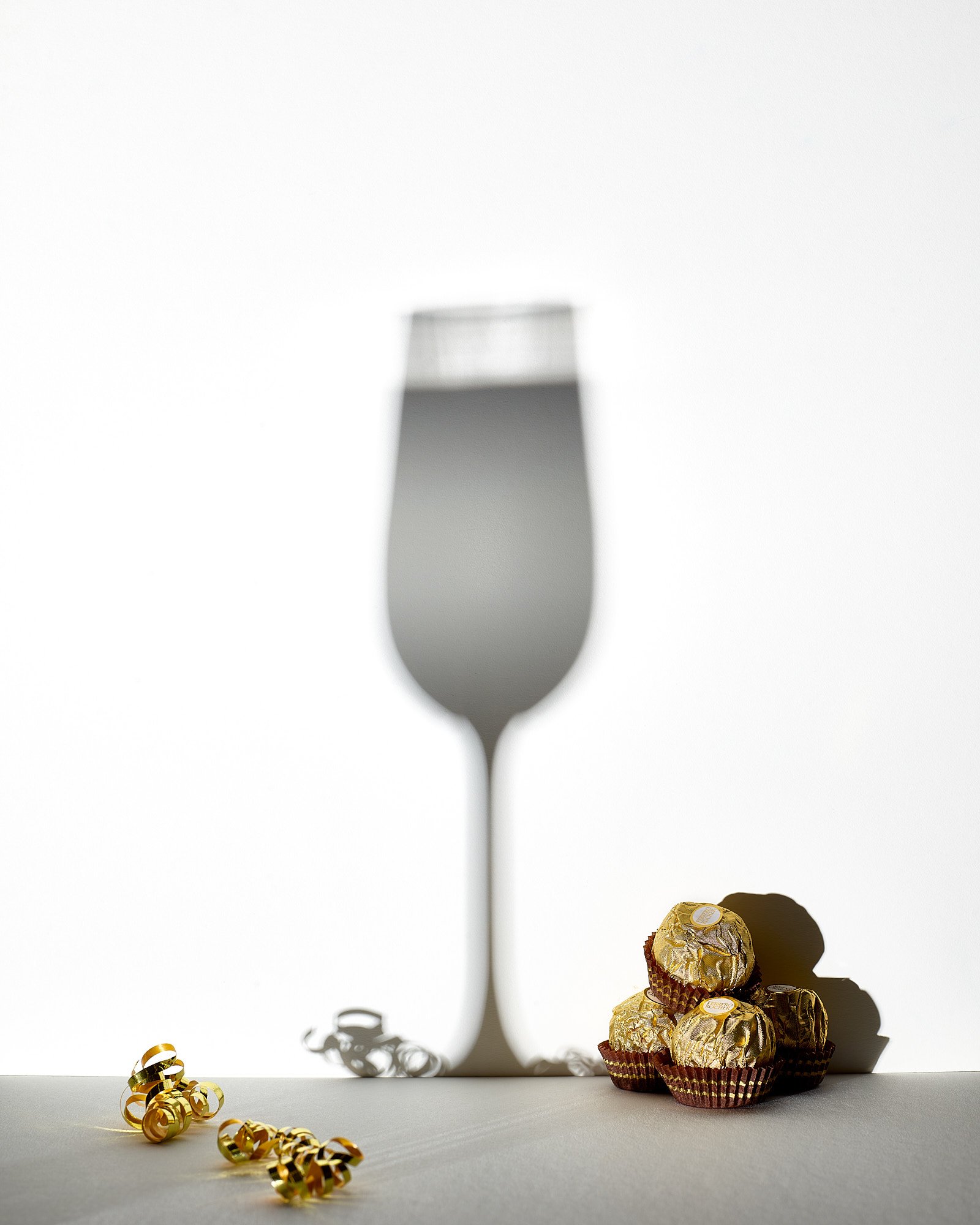 New Year's Eve champagne flute shadow Ferrero Rocher chocolate gold confetti minimal food advertising photography by Dhanraj Emanuel, studio food photographer Greensboro NC