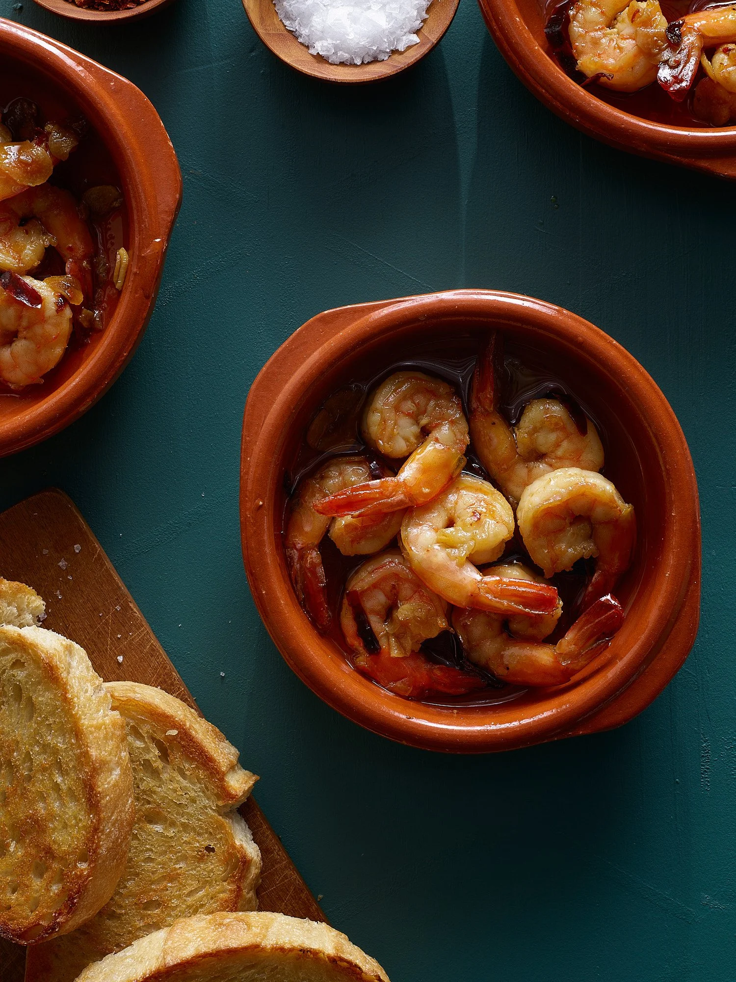 Food advertising photography by Dhanraj Emanuel — gambas al ajillo, shrimp in sauce with toasted bread on dark teal background. Commercial food photographer for restaurants and advertising agencies, available nationwide.