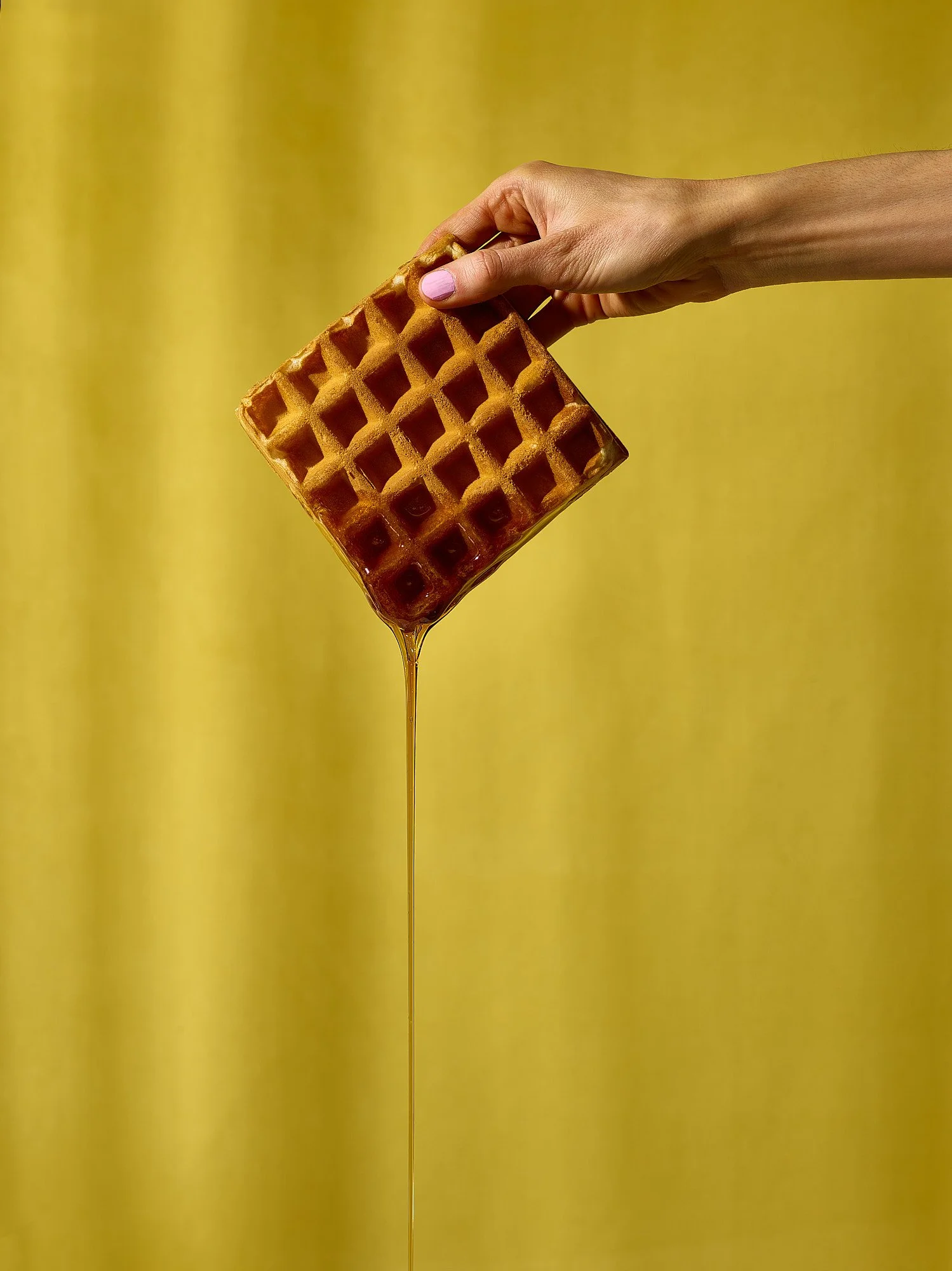 Waffle with honey drip hand holding committed yellow background food advertising photography by Dhanraj Emanuel, CPG food photographer Greensboro NC