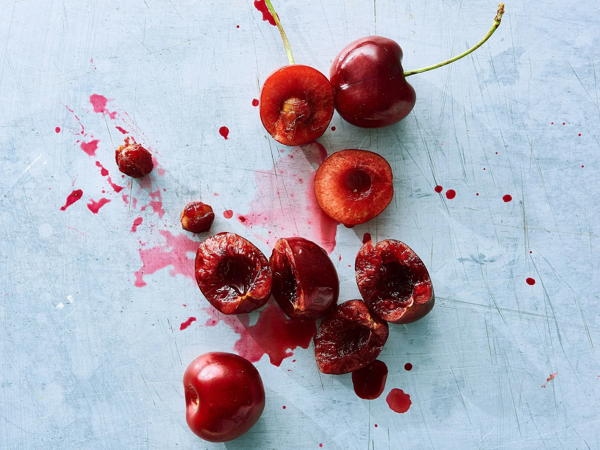 Smashed cherries red juice splatter light blue surface fine art food advertising photography by Dhanraj Emanuel, CPG food photographer Greensboro NC