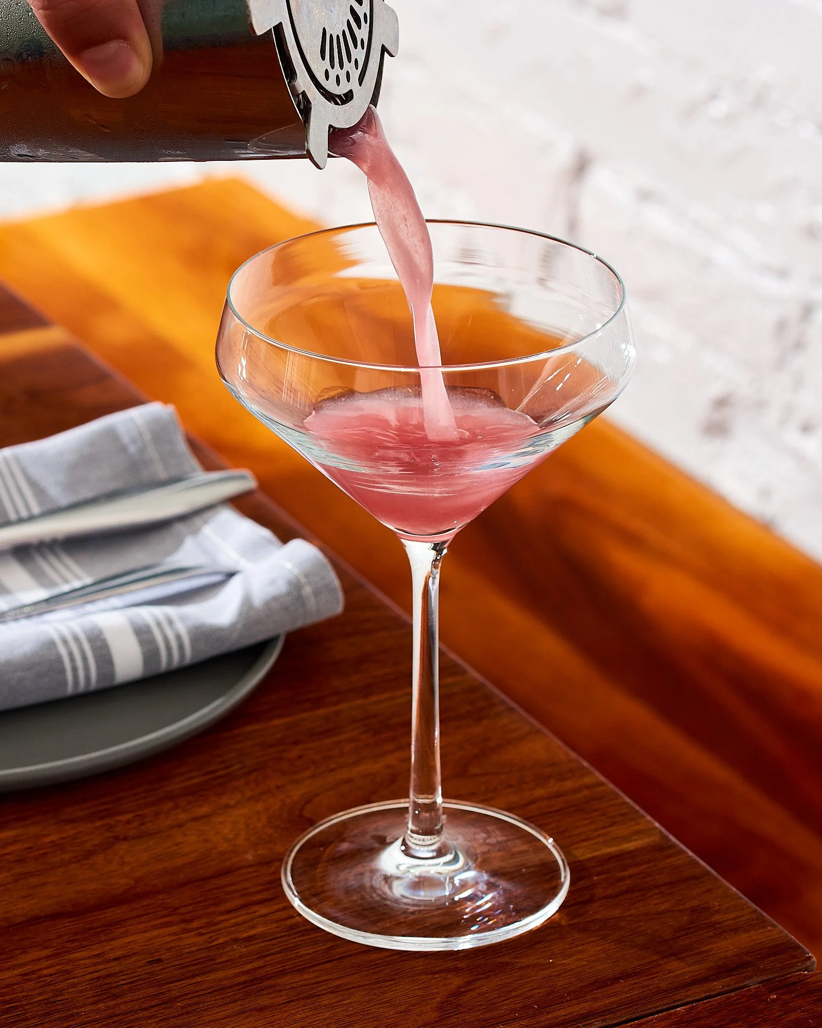 Beverage advertising photography by Dhanraj Emanuel — pink cocktail being poured into martini glass on wooden surface. Commercial drink photographer for spirits brands, restaurants, and advertising agencies, available nationwide.
