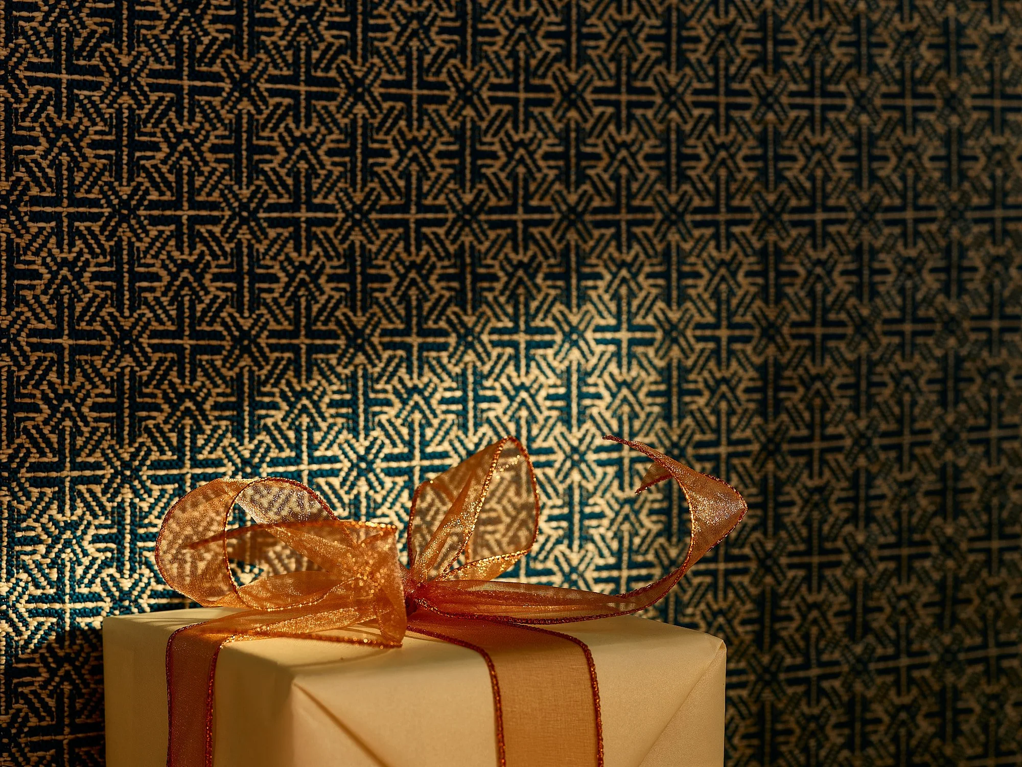 Commercial conceptual photography by Dhanraj Emanuel — elegantly wrapped gift with ribbon against dark patterned background, holiday campaign imagery. Advertising photographer for brands and agencies, working nationally.