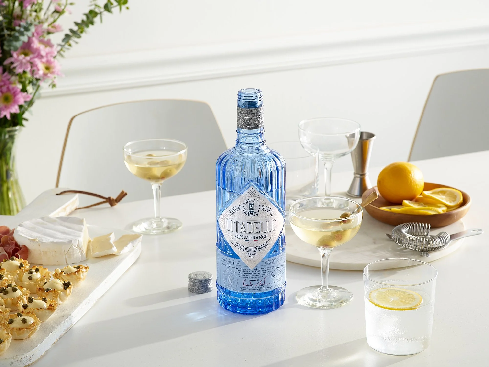 Beverage advertising photography by Dhanraj Emanuel — Citadelle gin bottle styled with cocktails, lemon, cheese board, and flowers. Commercial spirits photographer for beverage brands and advertising agencies, working nationally.