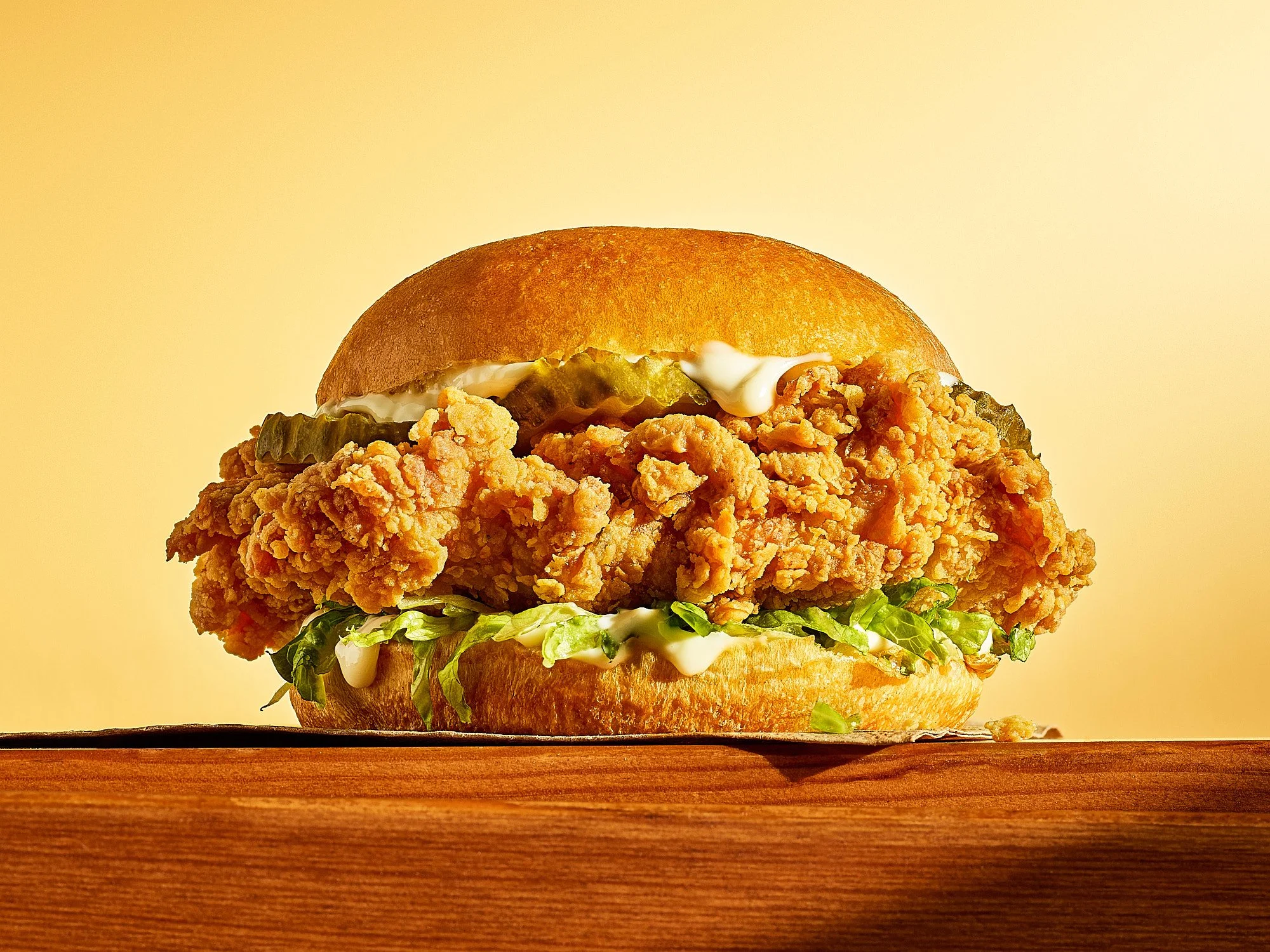 Fried chicken sandwich from popeyes warm gold surface dramatic food advertising photography by Dhanraj Emanuel, CPG food photographer Greensboro NC
