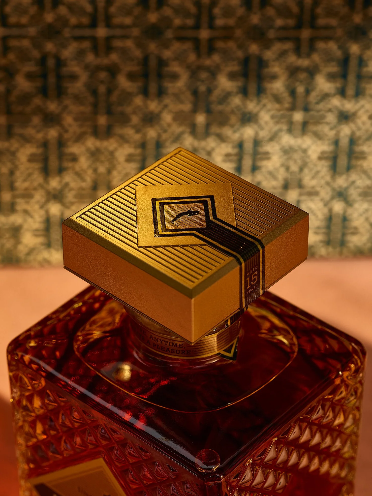 Spirits advertising photography by Dhanraj Emanuel — decorative spirits bottle with gold cap and fish logo detail against rich patterned background. Commercial beverage photographer for premium spirits brands and advertising agencies, working nationa