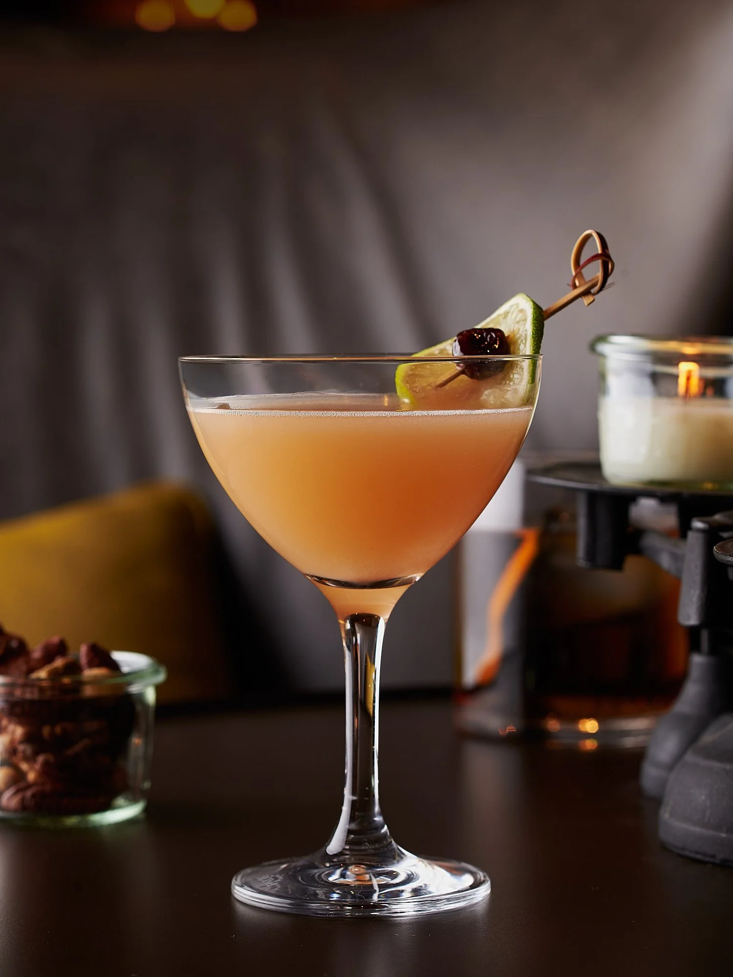 Amber cocktail in coupe glass with lime wedge and cherry garnish — commercial beverage photographer Dhanraj Emanuel | cocktail and spirits photography for restaurants and advertising agencies | available nationwide