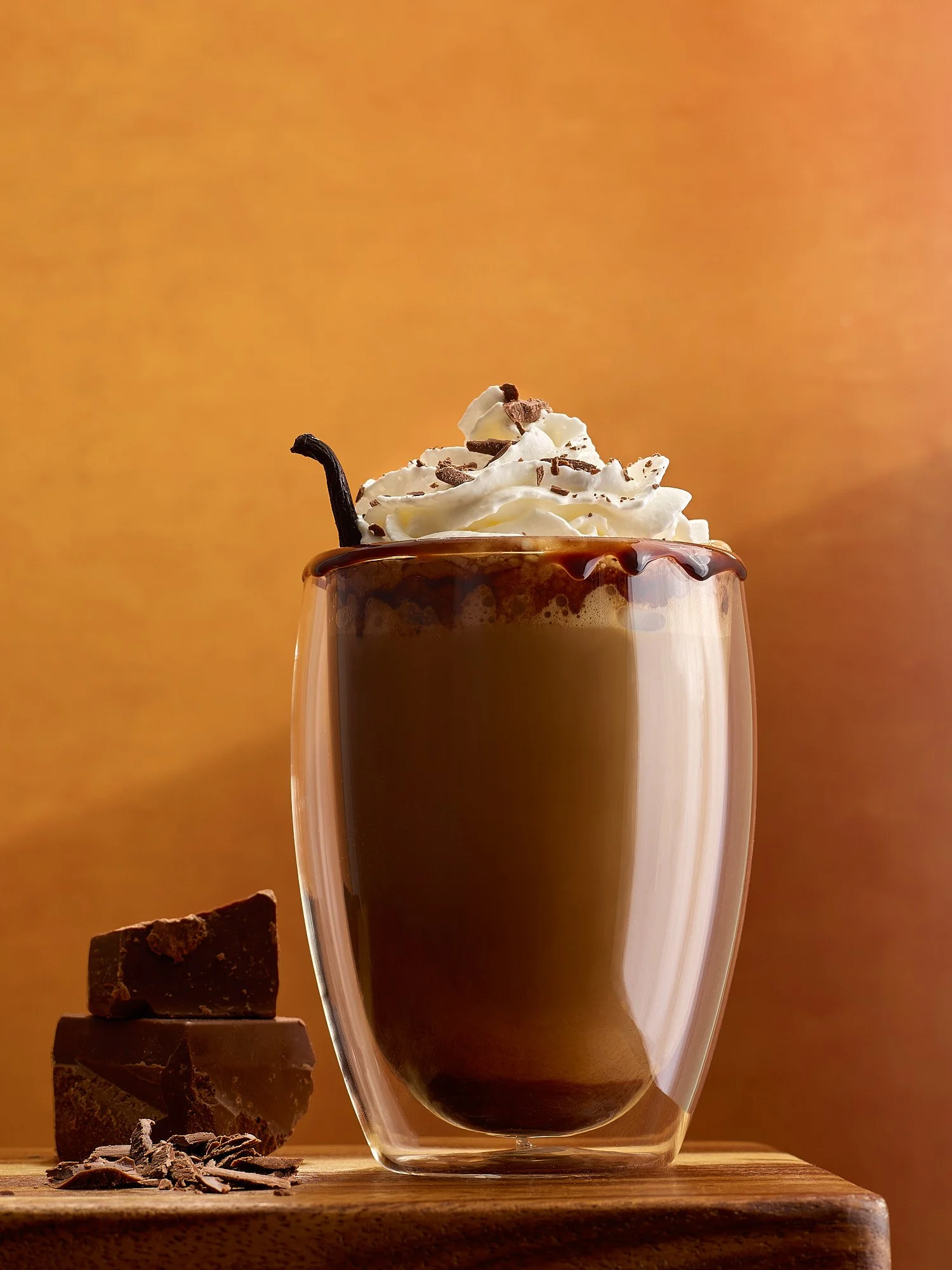 Beverage advertising photography by Dhanraj Emanuel — hot chocolate topped with whipped cream and chocolate shavings against warm amber background. Commercial drink photographer for CPG and beverage brands, working nationally.