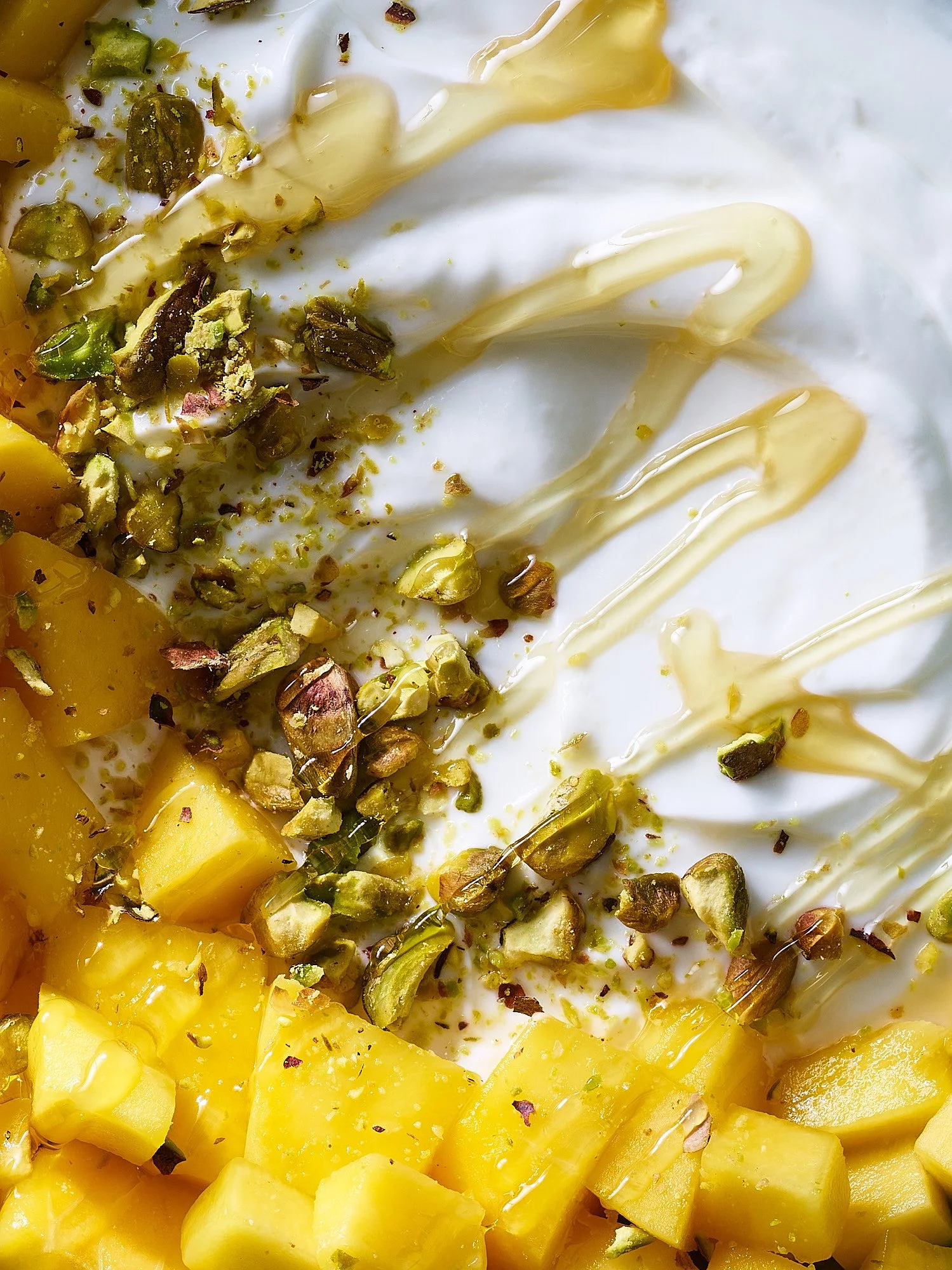 yogurt with diced mango, chopped pistachios, yogurt, and honey drizzled on top.