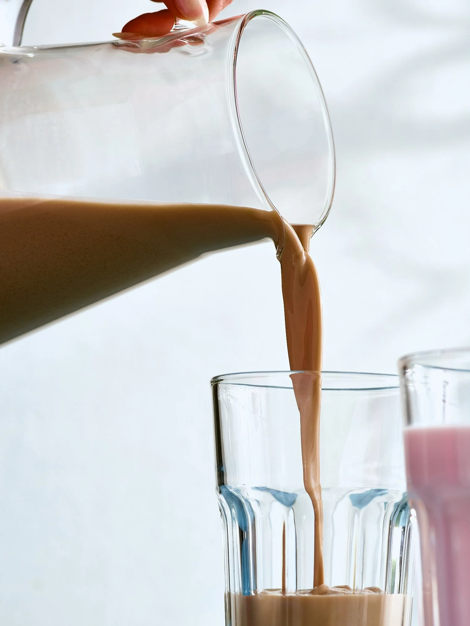 Beverage advertising photography by Dhanraj Emanuel — chocolate milk poured from glass pitcher into clear glass. Commercial drink photographer for CPG and dairy brands, working nationally for agencies and grocery clients.
