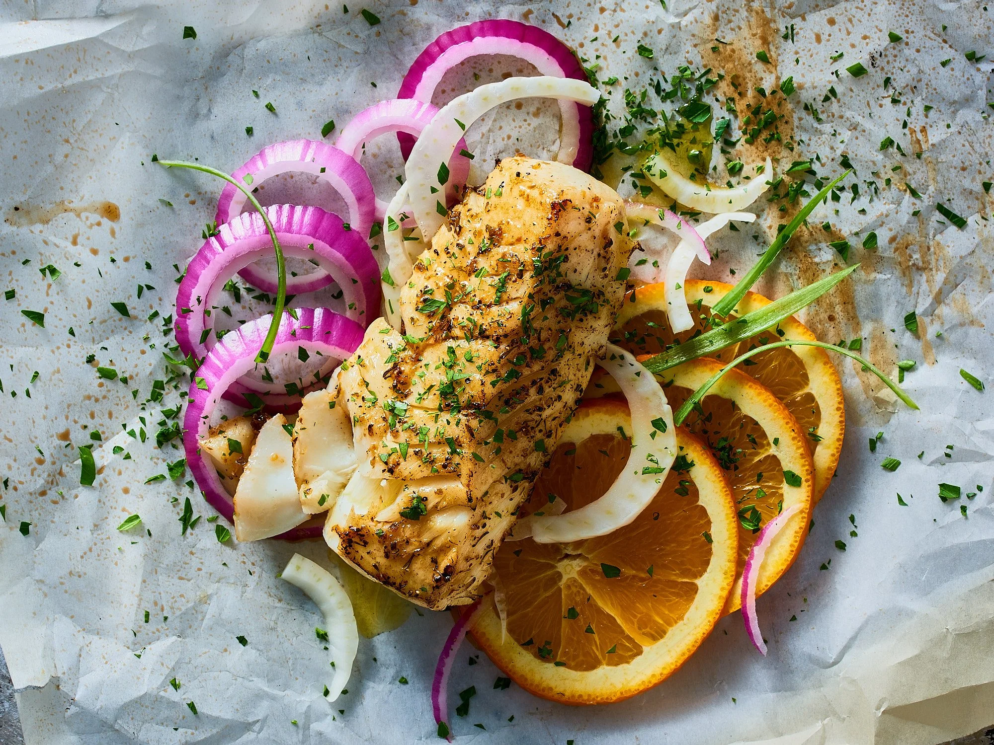 Food advertising photography by Dhanraj Emanuel — grilled fish fillet with citrus, red onion, and herbs on parchment, shot for The Fresh Market. Commercial food photographer based in Greensboro NC, available nationwide.