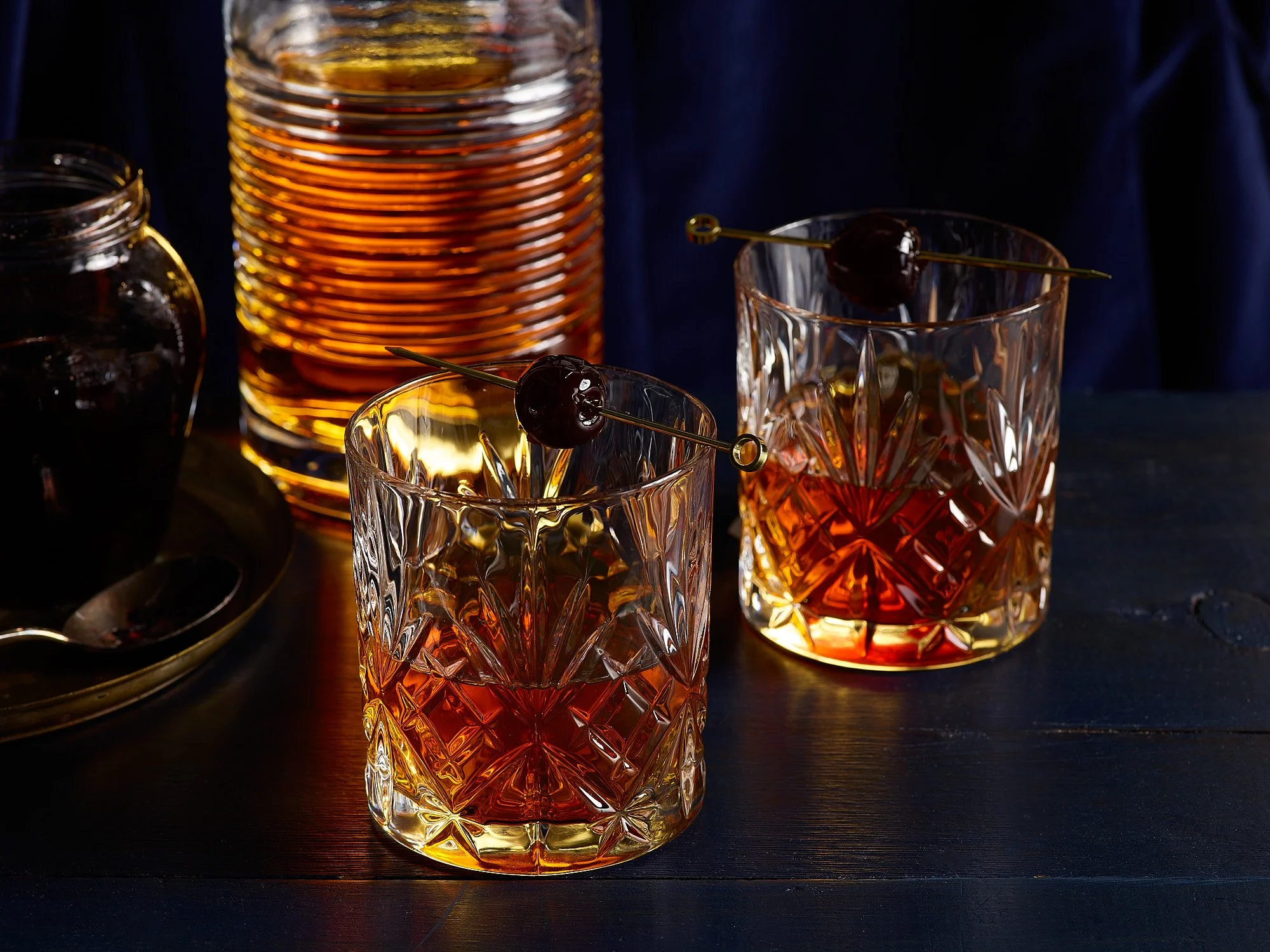 TSpirits advertising photography by Dhanraj Emanuel — two whiskey cocktails with cherry garnish on dark wooden surface. Commercial beverage photographer for spirits brands and advertising agencies, working nationally.