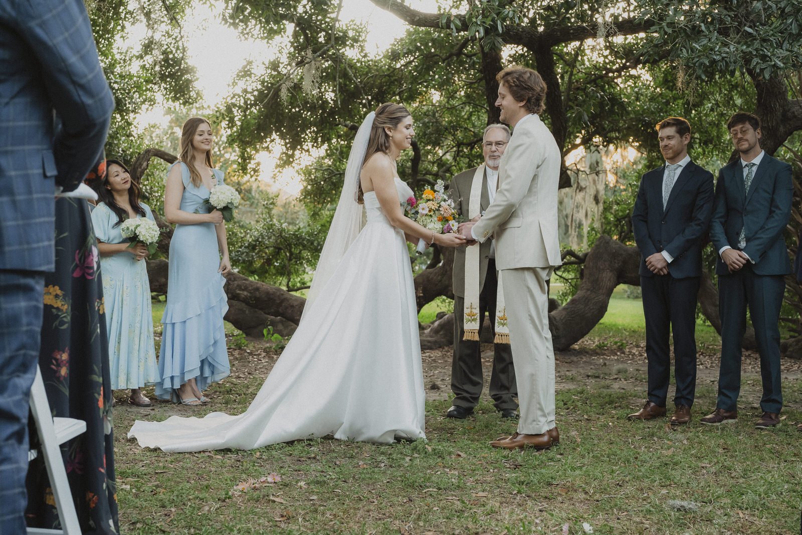 Couple exchanges vows beneath a large oak tree during an outdoor spring wedding ceremony.