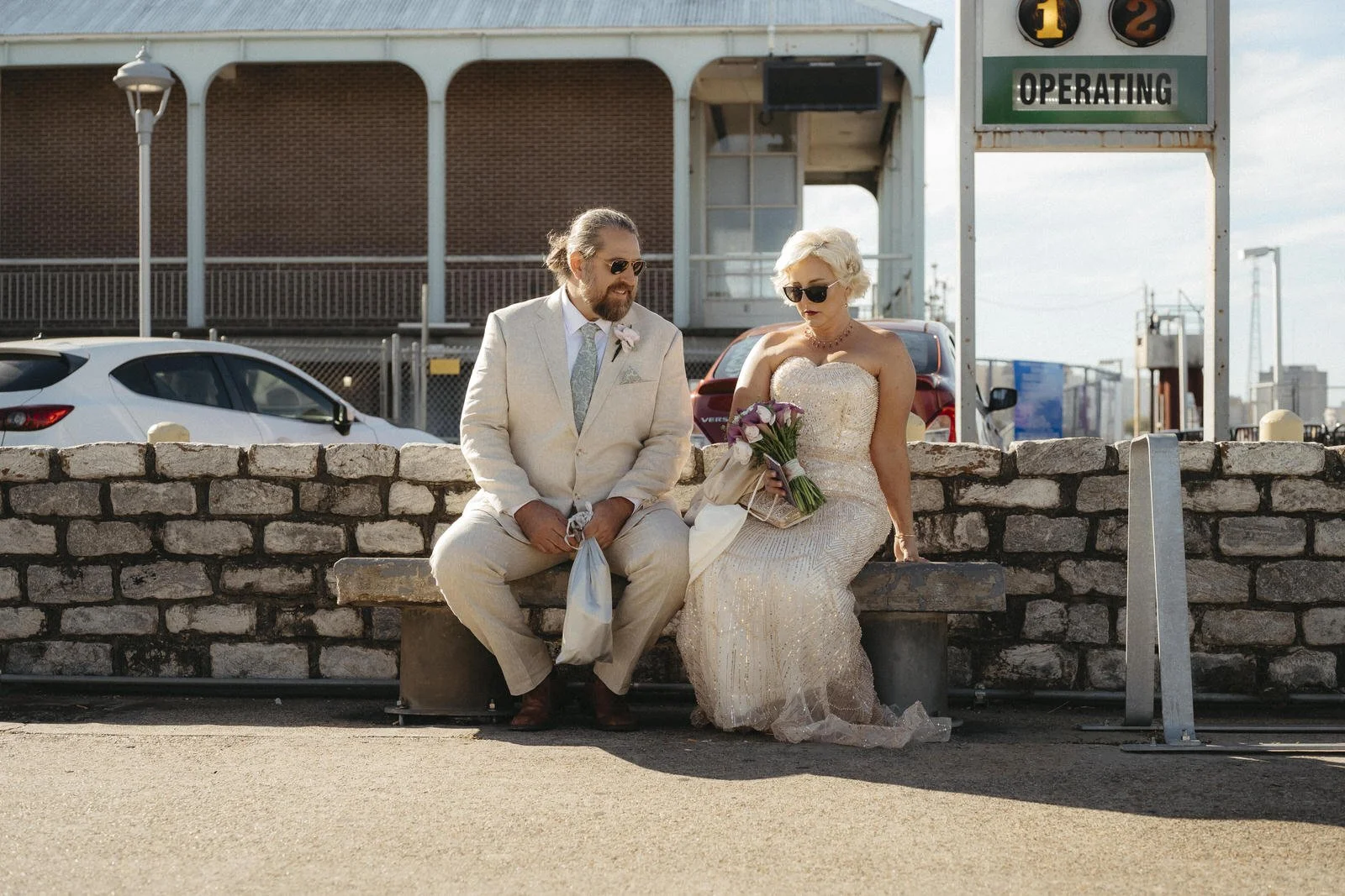 Newlywed couple shares a quiet candid moment while sitting together on a brick wall.