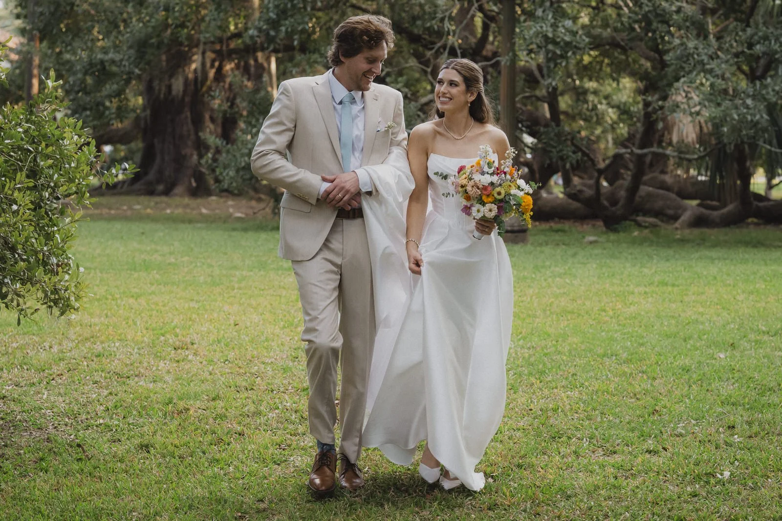Bride and groom walk together through a garden during relaxed wedding portraits.