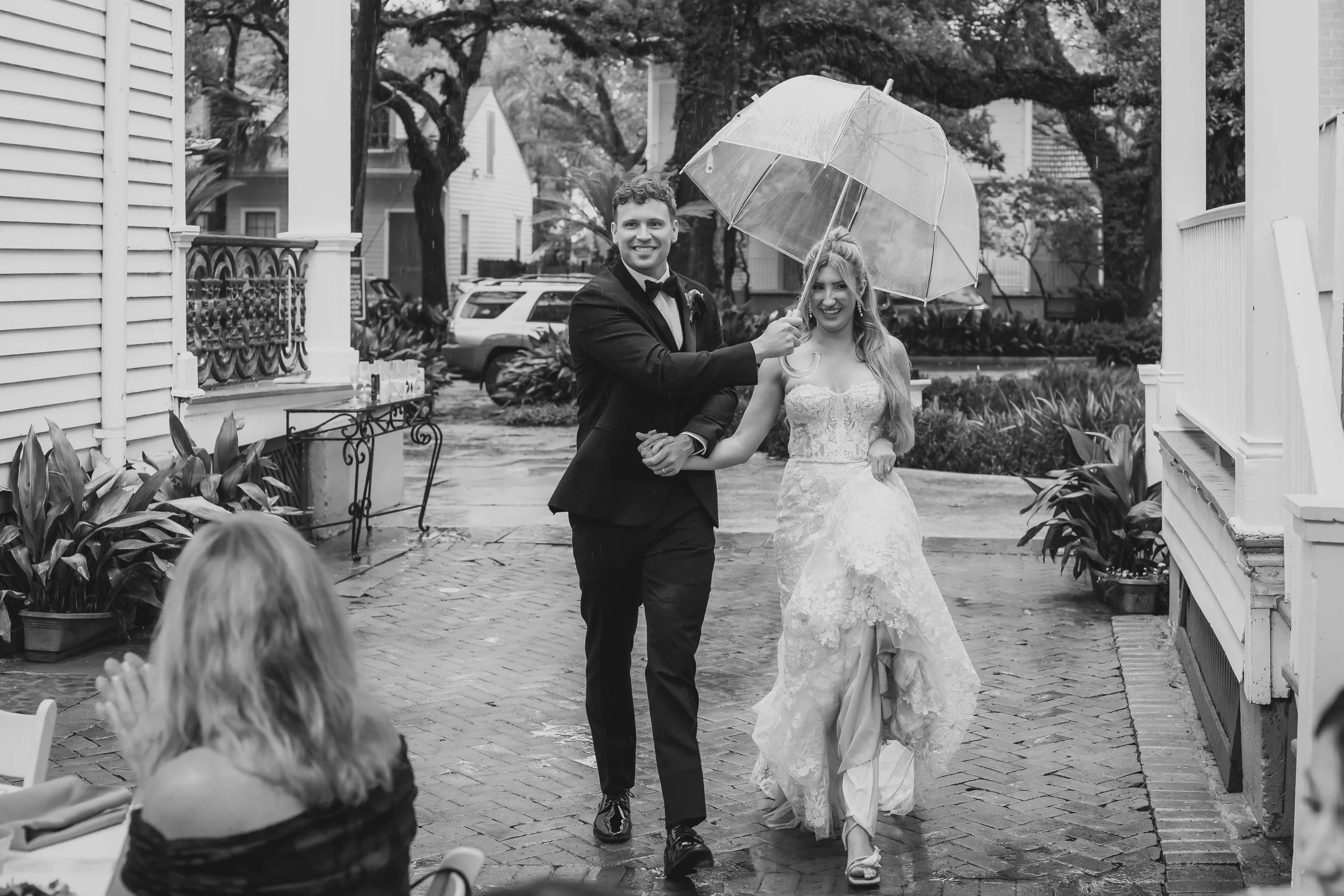 Newlyweds walk through a New Orleans courtyard beneath an umbrella during the rain.