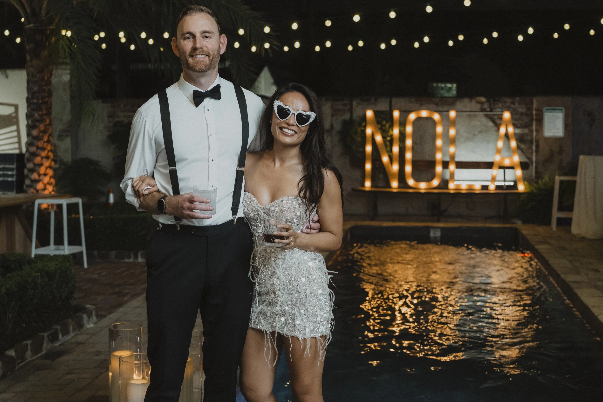 Newlyweds pose beneath a glowing NOLA sign during their wedding reception.