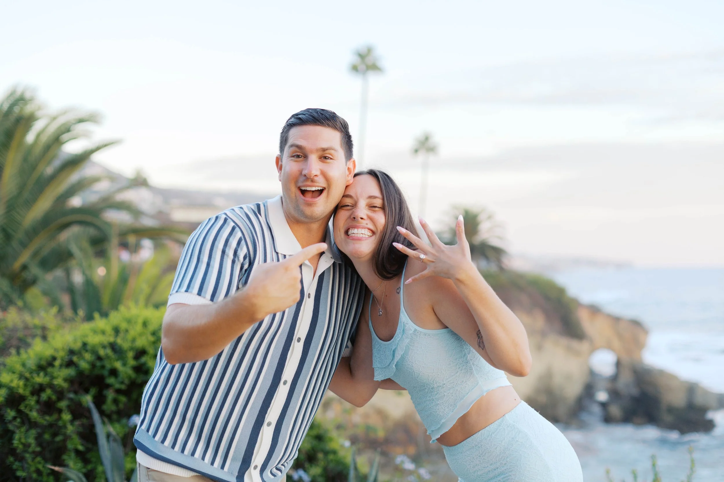 Andrew and Chloe celebrating their engagement with the Laguna Beach coastline behind them