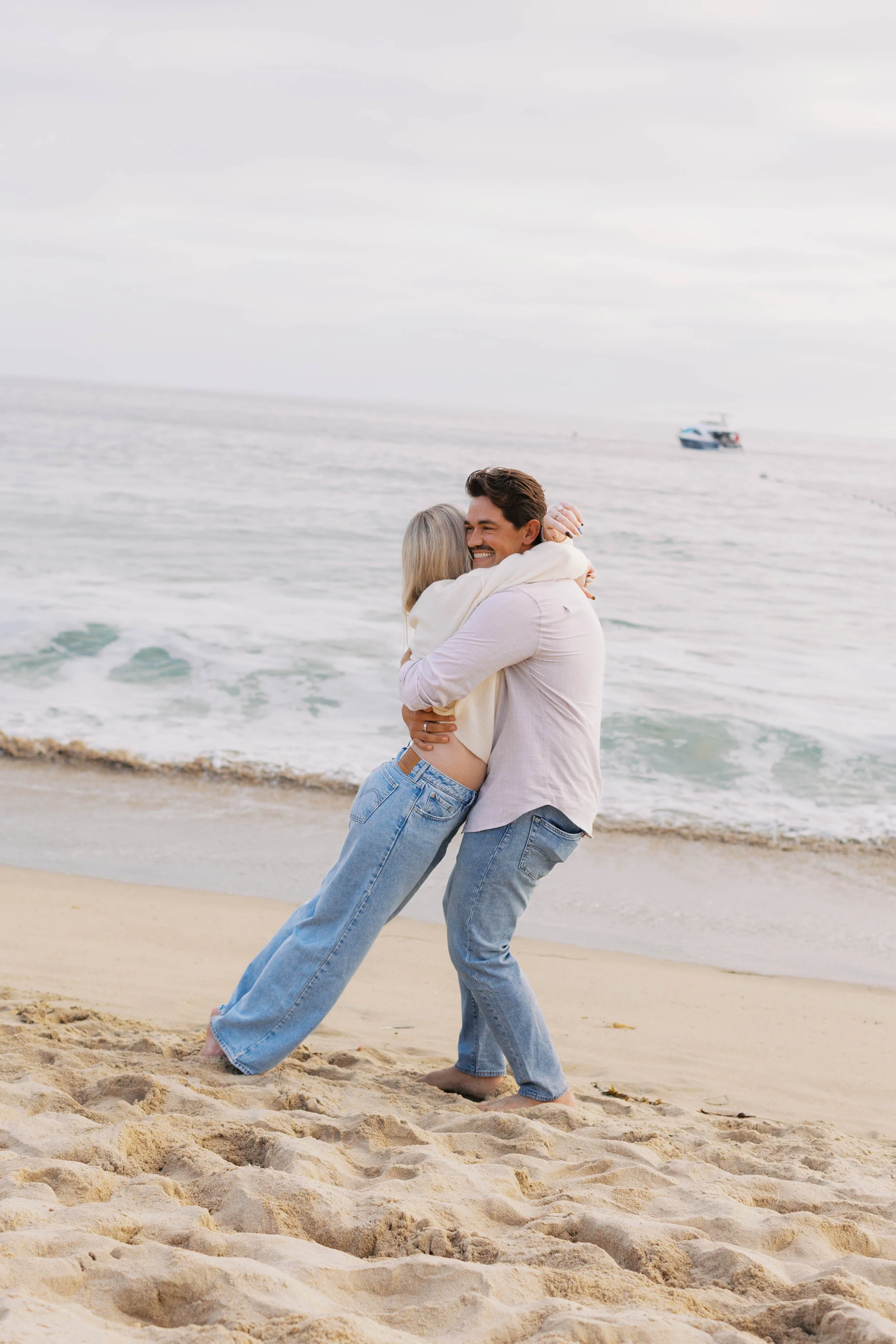 Newly engaged couple celebrating with a joyful hug after their Emerald Bay beach proposal in Laguna Beach.