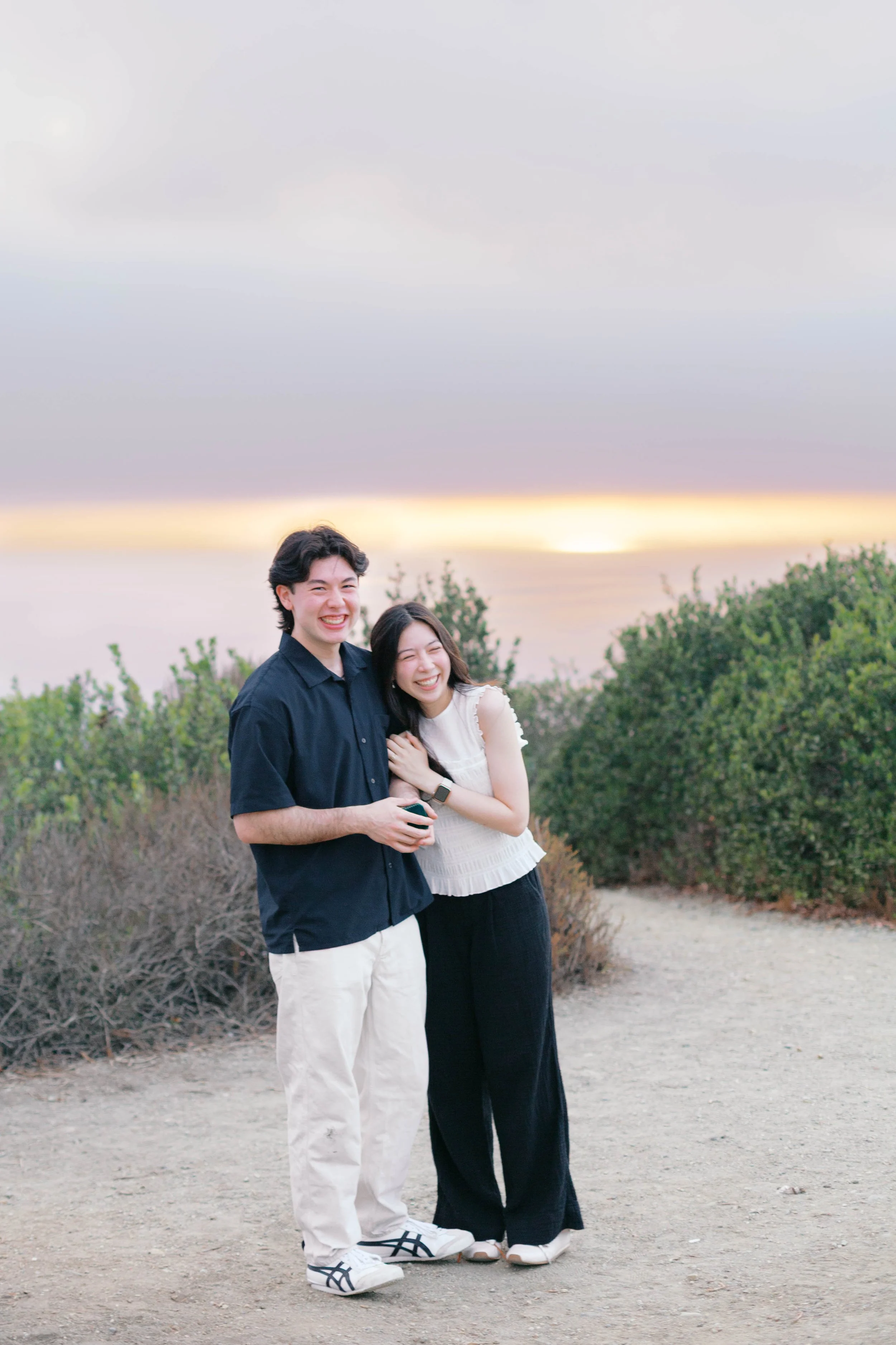 Curtis and Eimi smiling together after their sunset proposal near Laguna Beach.
