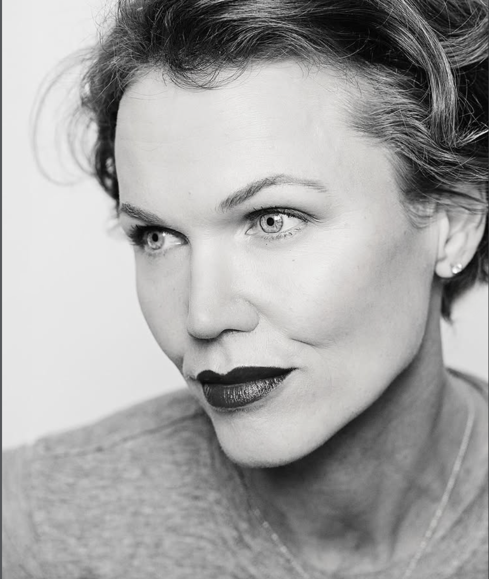 A close-up black and white portrait of a woman with short, wavy hair and light-colored eyes, looking slightly to her left with a confident expression.