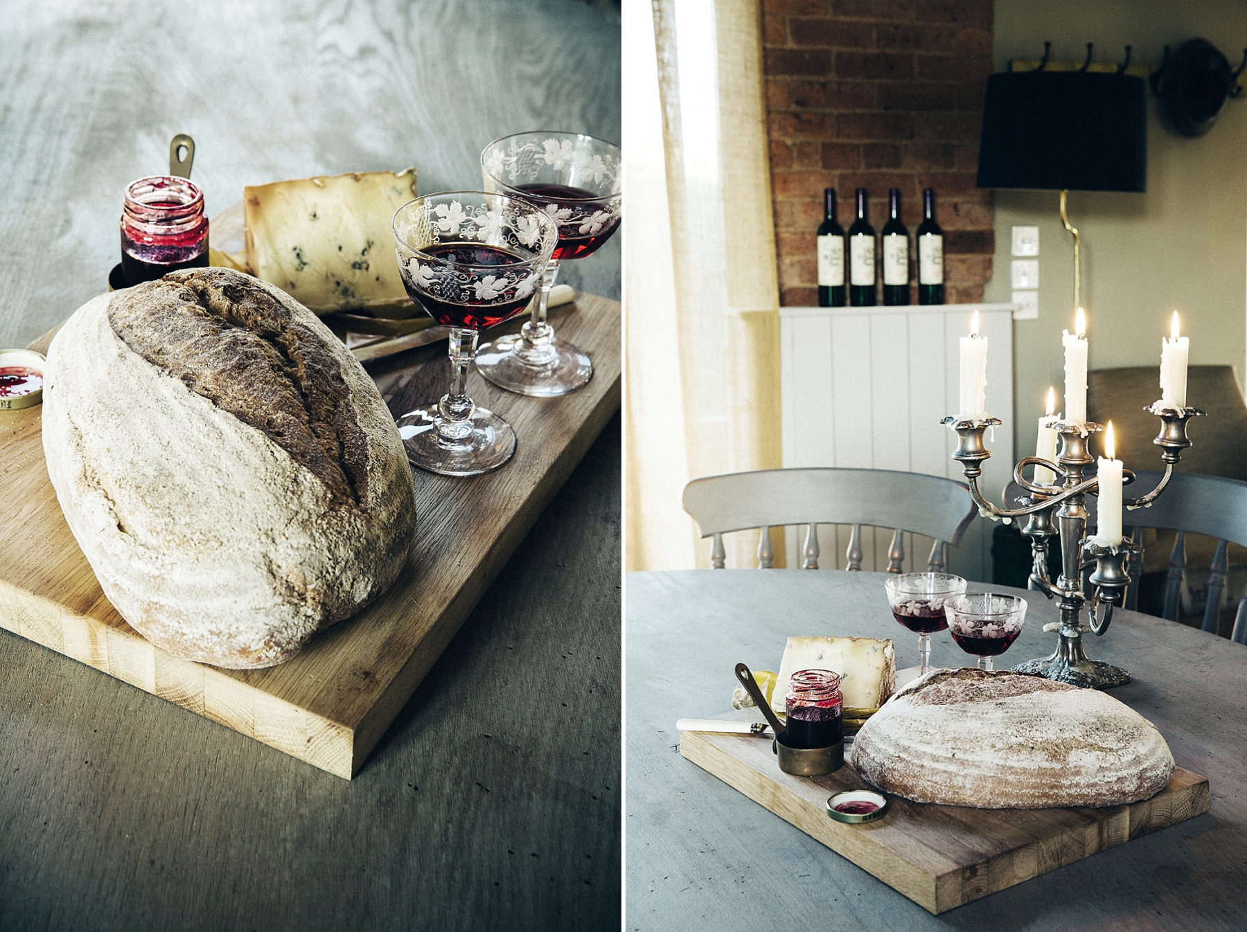 A round loaf of bread, two glasses of red wine with intricate floral patterns, a wedge of cheese, and jars of berry jam on a wooden serving board, set on a wooden table.