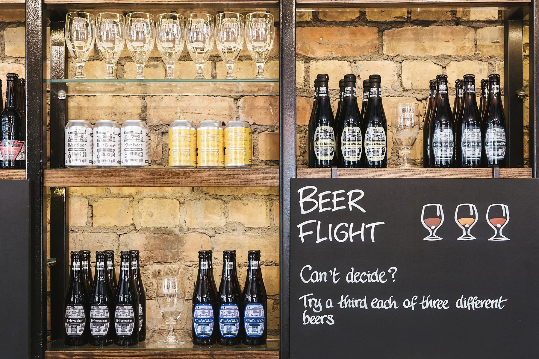 Shelves with various beer bottles and cans, including Stella Artois, and a chalkboard sign reading "Beer Flight" with instructions to try three different beers.