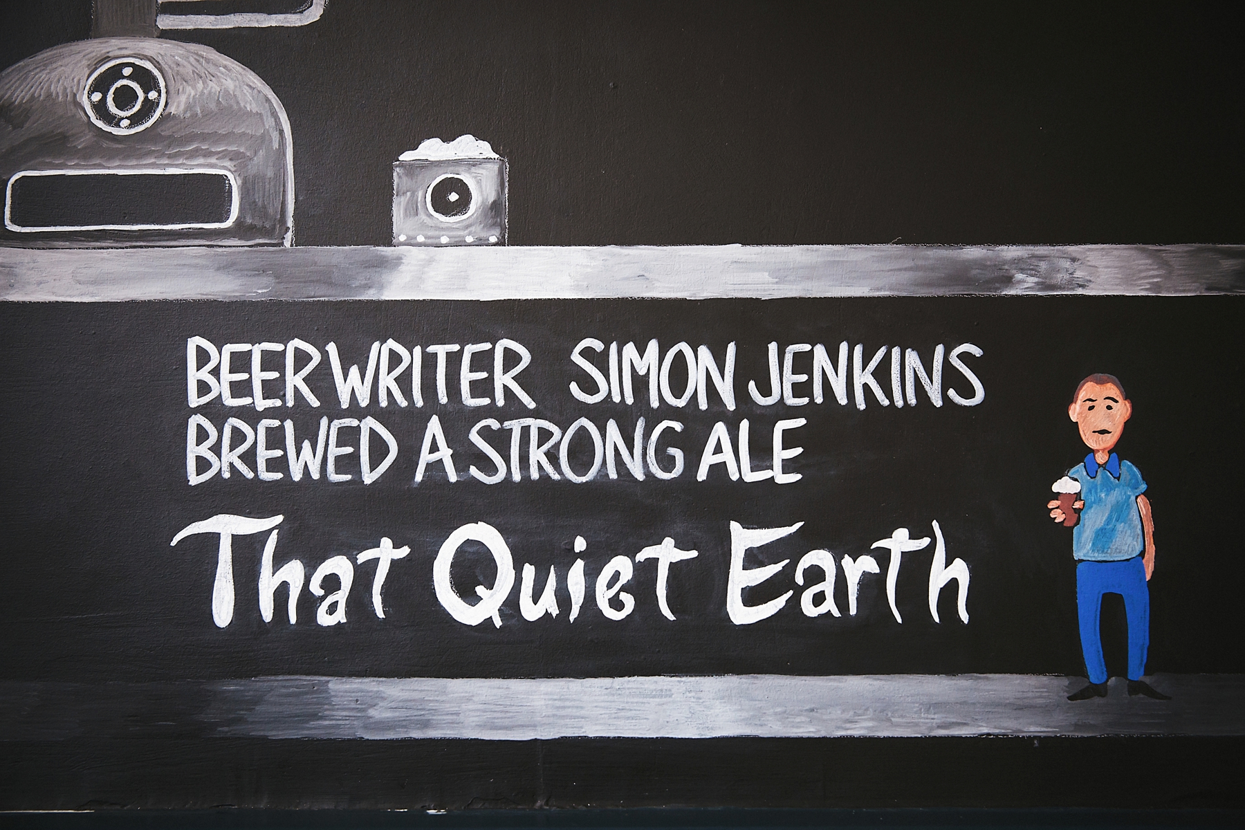 A blackboard-style wall with a drawing of a beer bottle, can, and a man holding a beer. The text on the wall reads: "Beer writer Simon Jenkins brewed a strong ale that quiet earth."
