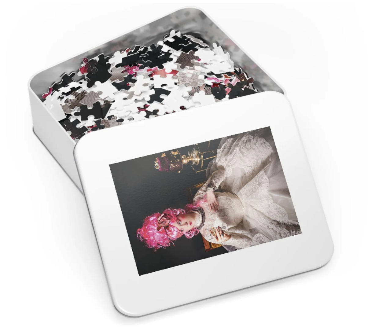 A white tin box with a picture of a woman with pink curly hair in fancy lace clothing on the lid. The box contains scattered jigsaw puzzle pieces.