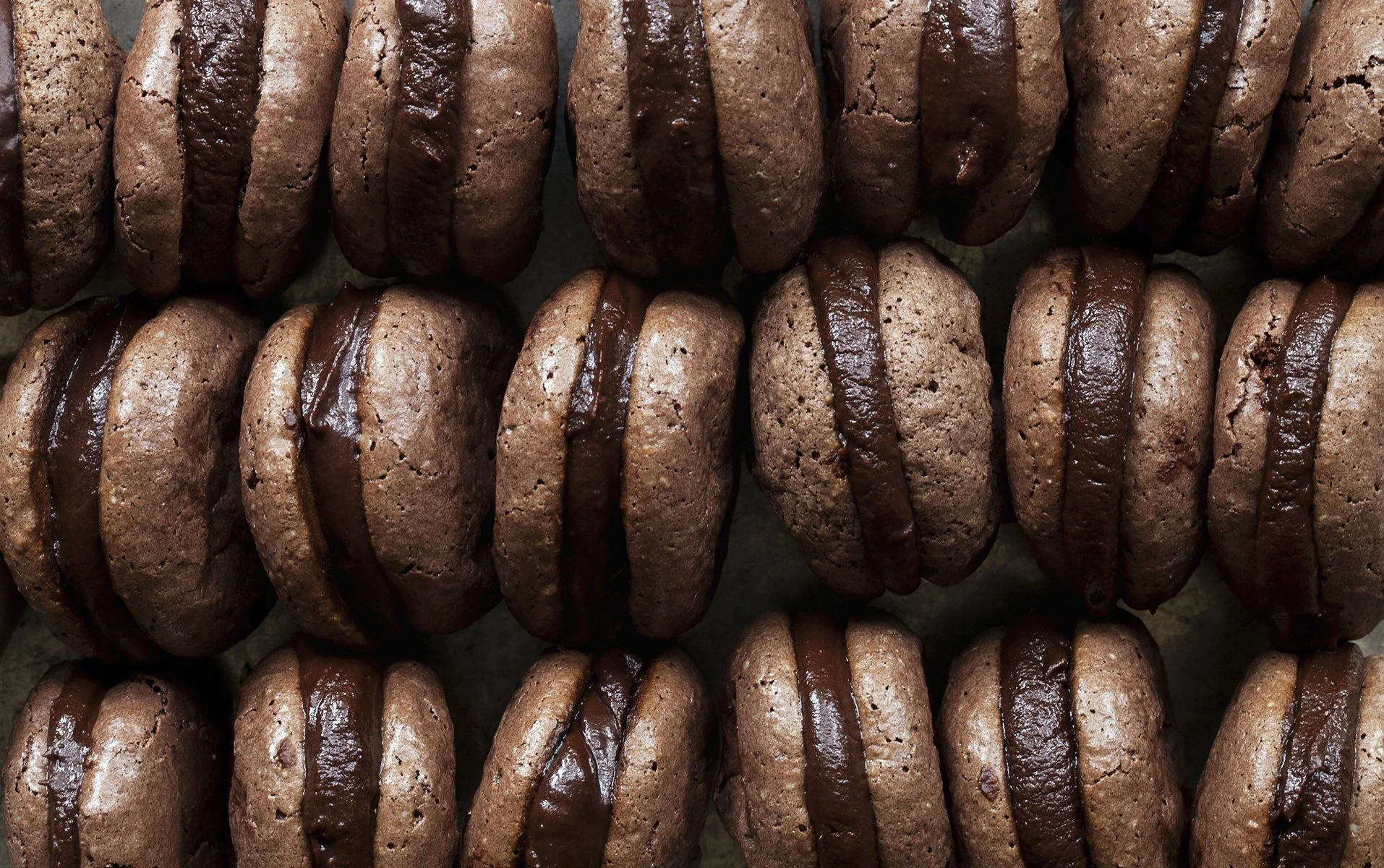 Close-up of chocolate macarons with a rich chocolate filling, arranged in rows.