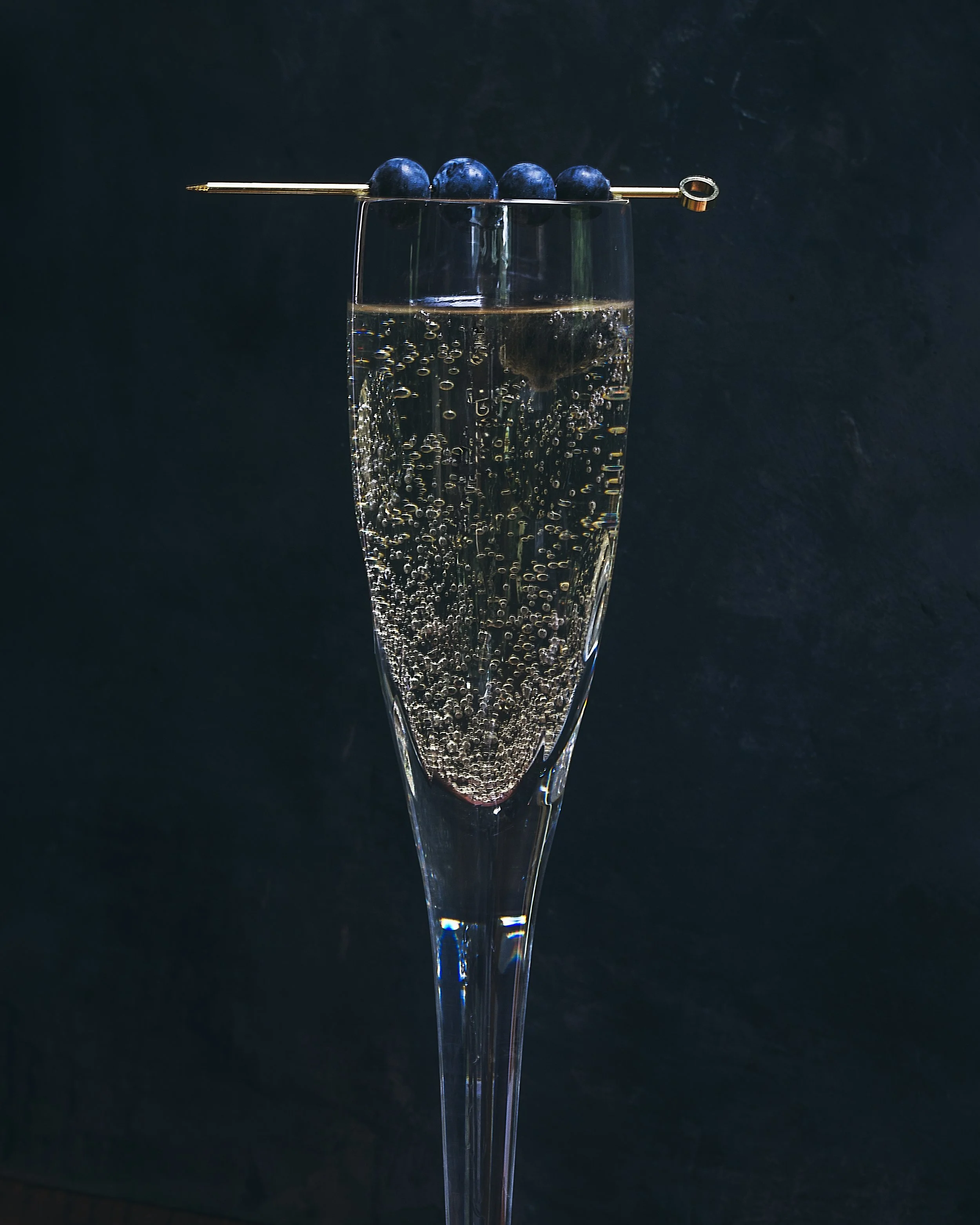 A champagne flute filled with sparkling water or champagne, topped with a skewer of blueberries resting across the rim.