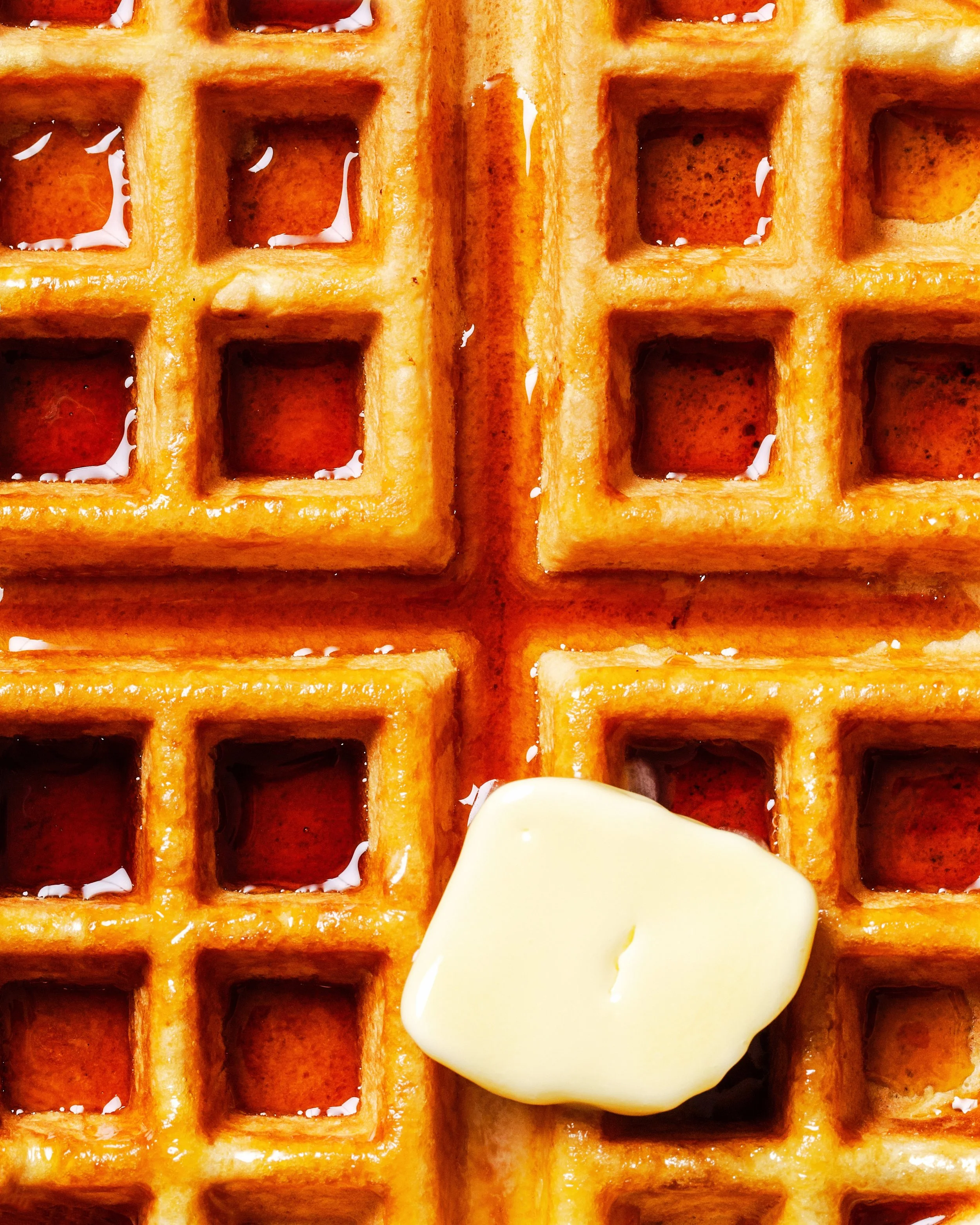 Close-up of two golden-brown waffles with a pat of melting butter and syrup.