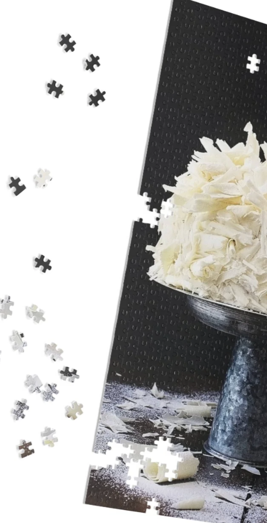 Jigsaw puzzle pieces, some assembled on black background and scattered on white surface, with a partially completed puzzle depicting a bowl of whipped cream.