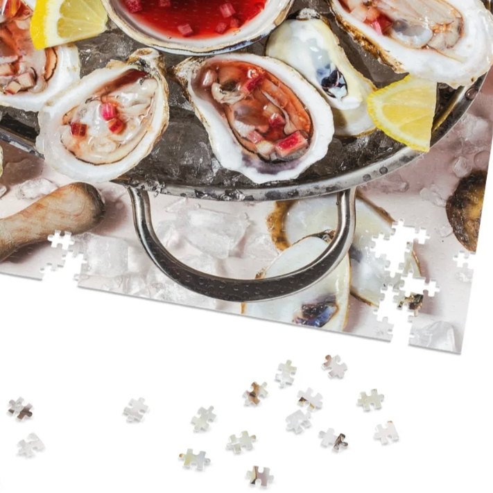 Fresh oysters on a silver tray with lemon wedges, surrounded by scattered puzzle pieces on a table.