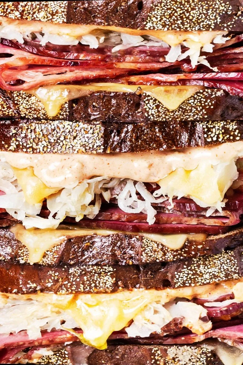 Close-up of a stack of sandwiches with various meats, cheeses, and toppings on toasted bread.