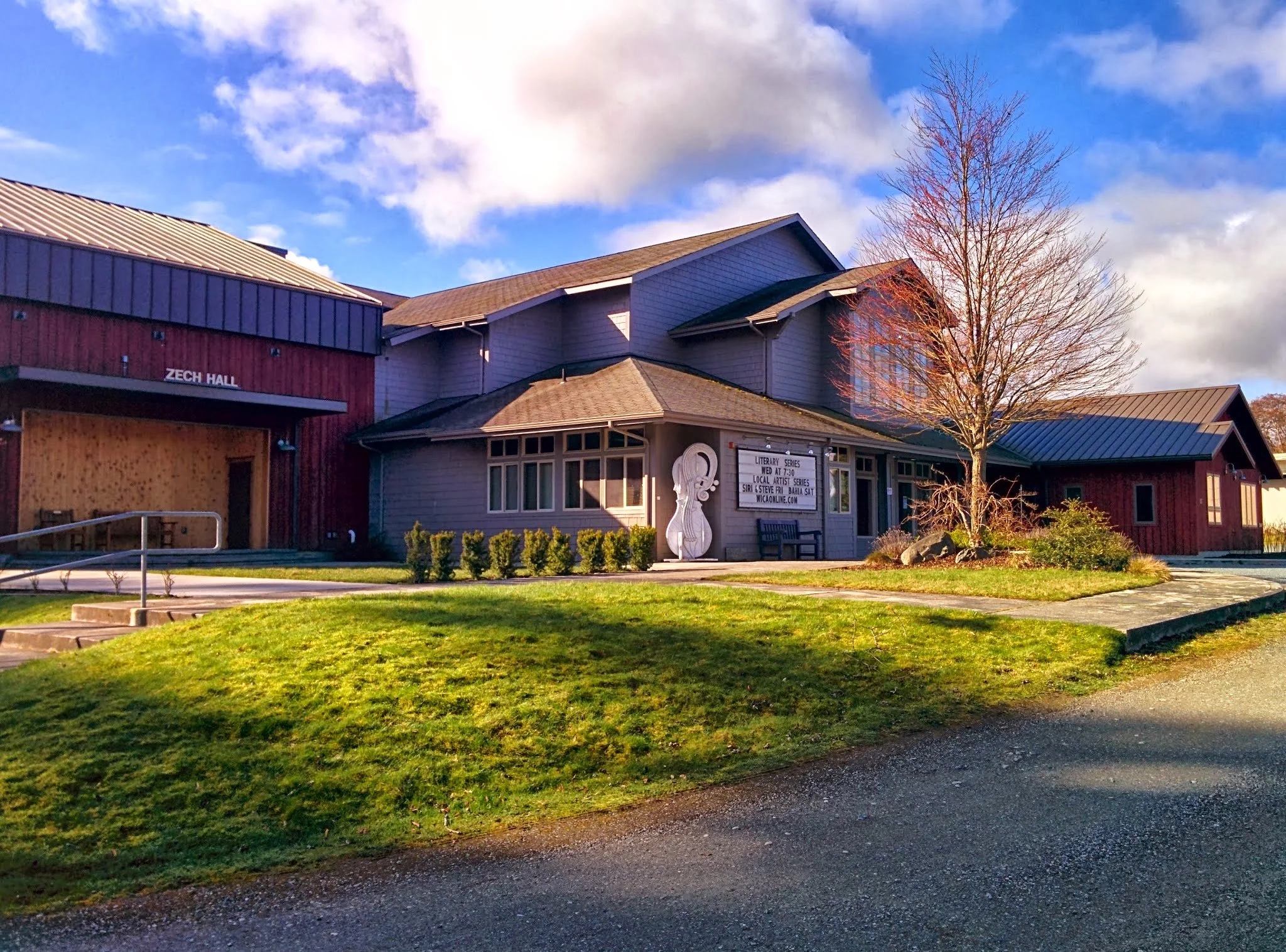 Image of WICA on a sunny day, grass in the front, Zech Hall in the back, large cello scultpture against the wall