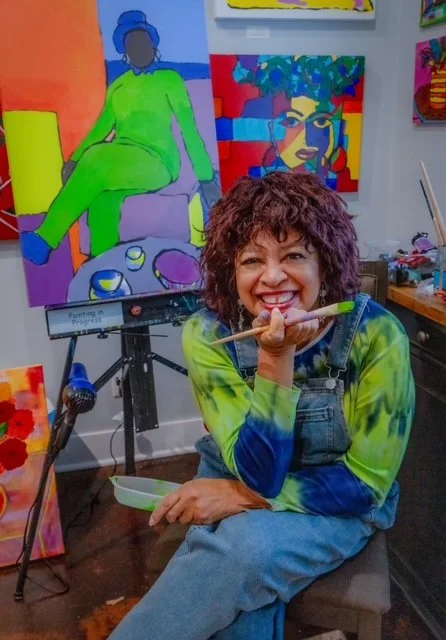 Pamelagrace Beatty in her studio with a paintbrush, painting in the background