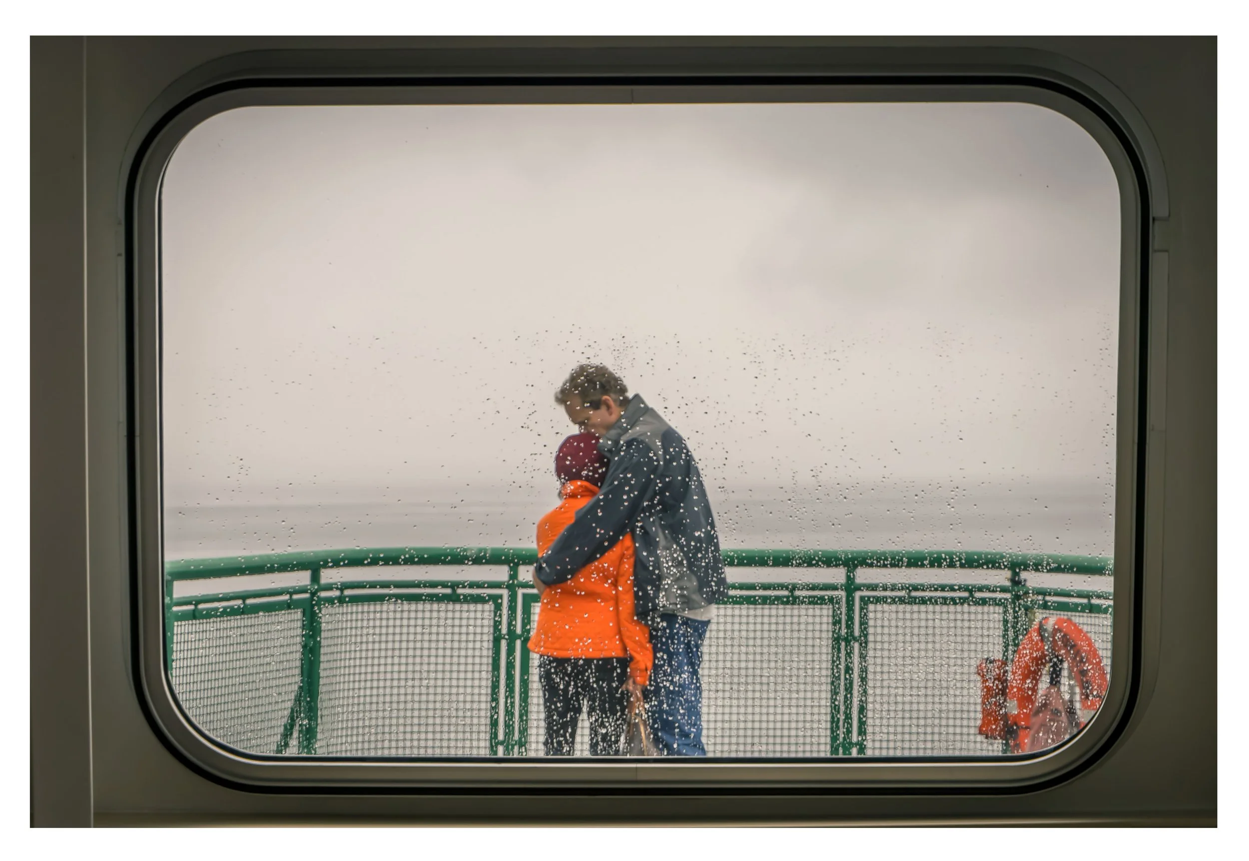 Two people embracing outside the ferry window, rain on window