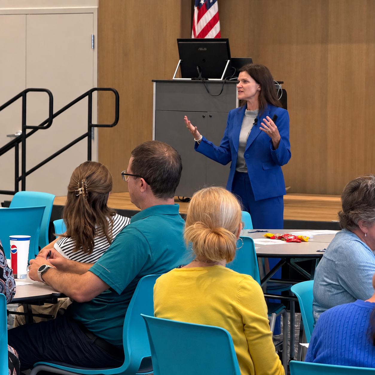 Sarah Ciavarri in a blue suit delivering a leadership presentation to participants seated at tables.