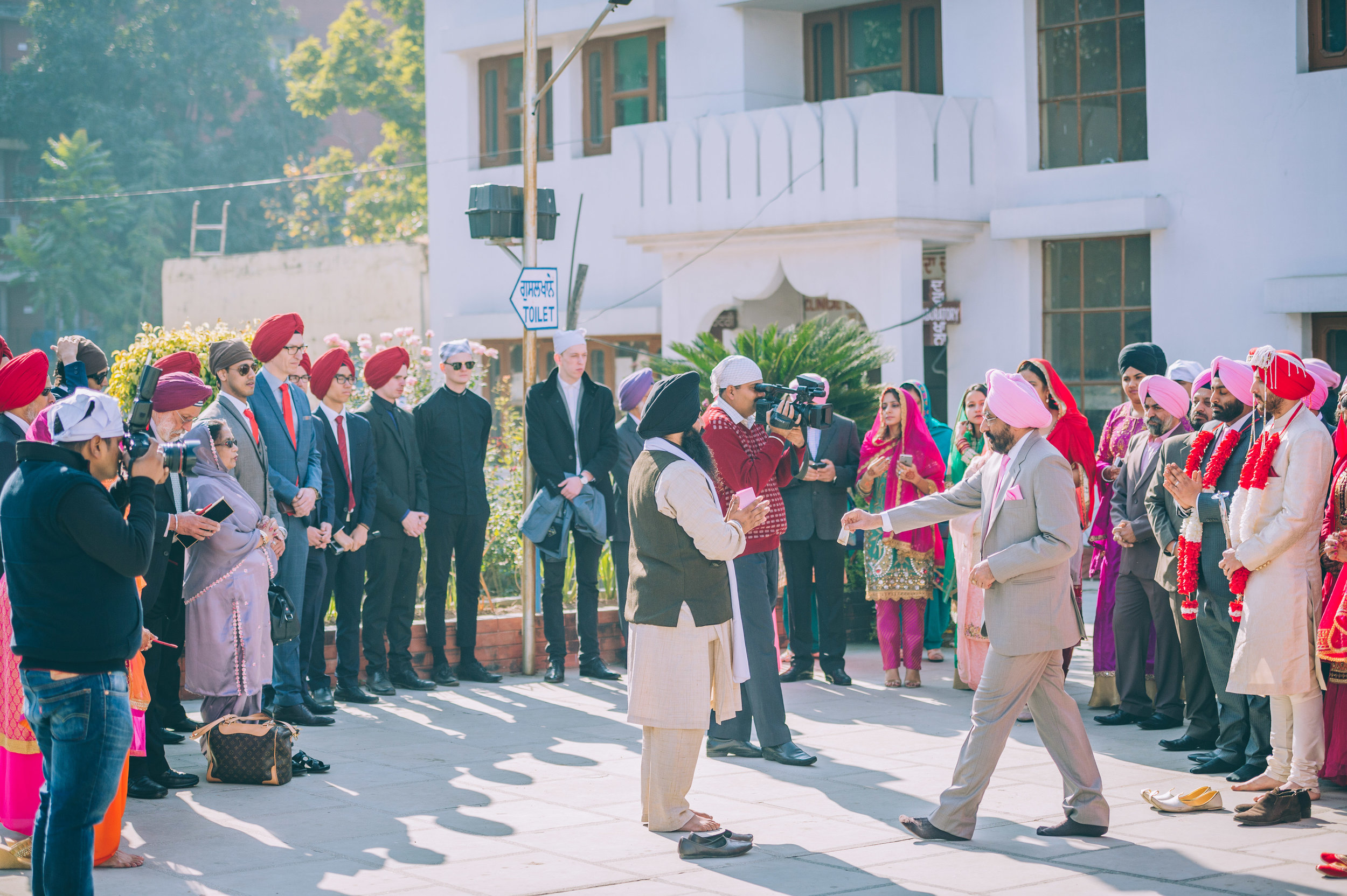  Families of the bride and groom gather for the  milni  (meeting). The priest (middle of the picture in a black turban) will then call out names of relatives from each side (beginning with the eldest) to put on a haar (garland) on each other. 