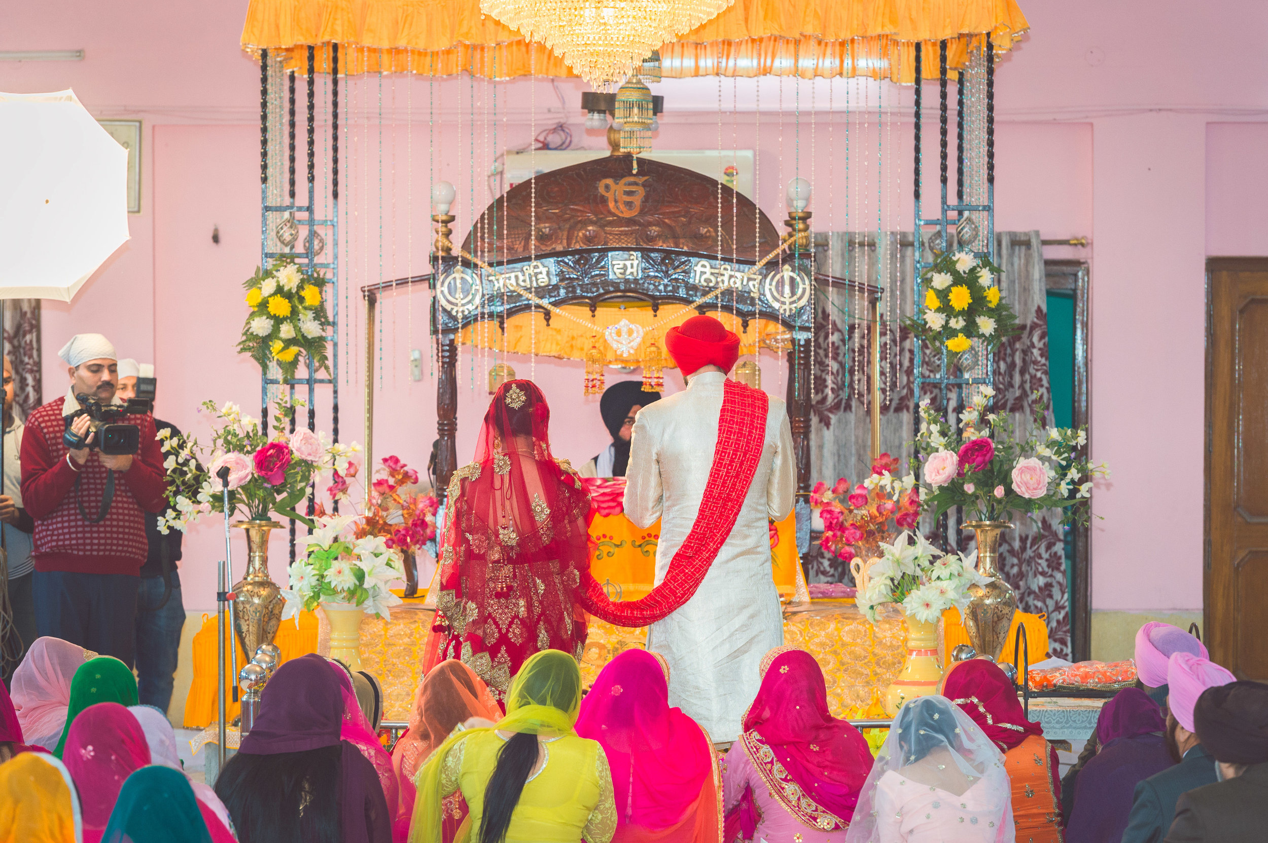  Bride and Groom standing in-front of the altar. The red scarf that is draped down the shoulders of the groom is called a  palla . It's the link between the couple as they journey around the altar. 