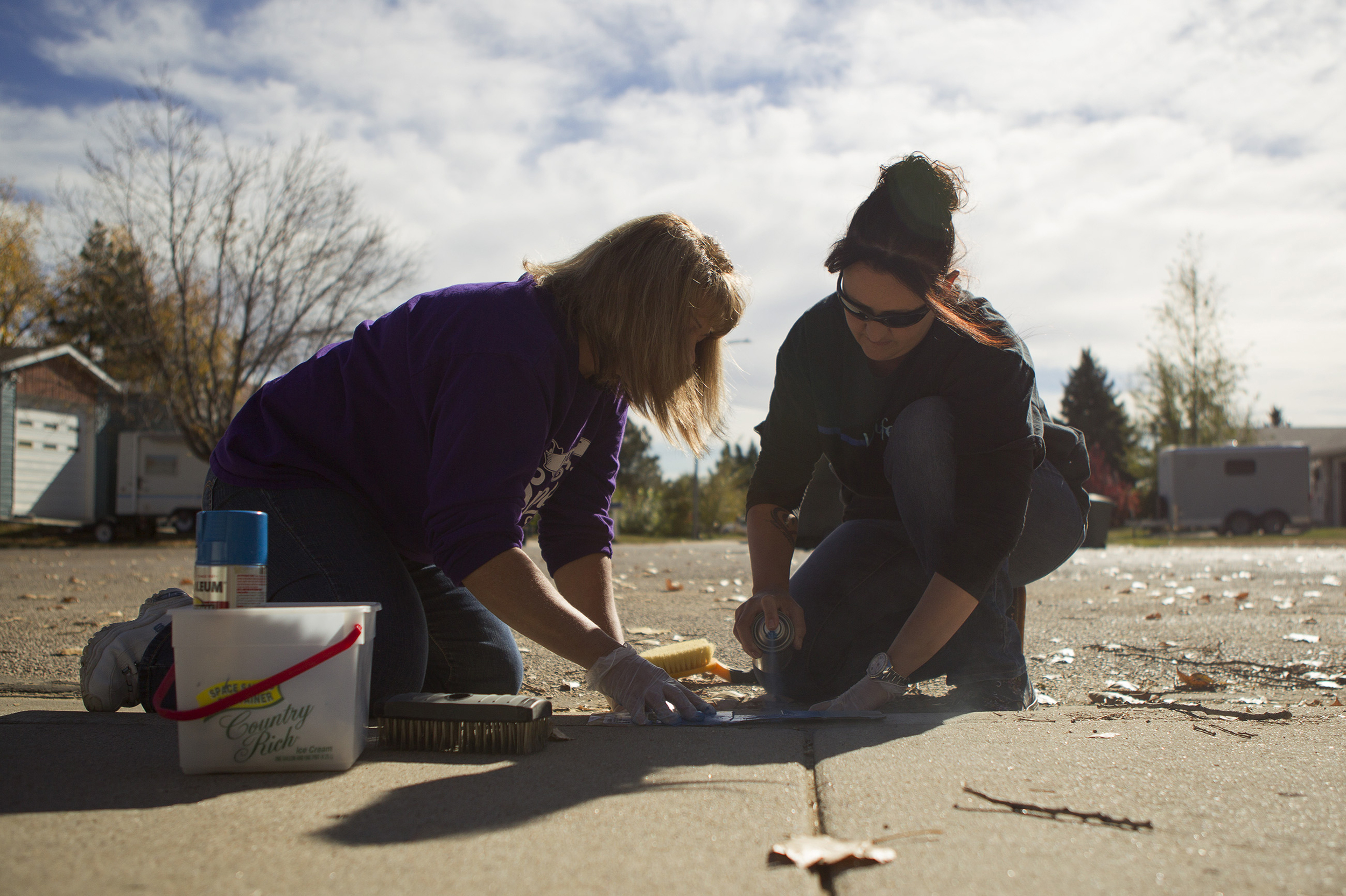 Maryann Hannigan, left, and Tonya Stroup paint a blue stripe Wednesday afternoon, on the curb of a neighbor's house on Alberta Drive. The blue stripes are part of a fundraiser for Shop with a Cop, and are meant to show support for local police officers.