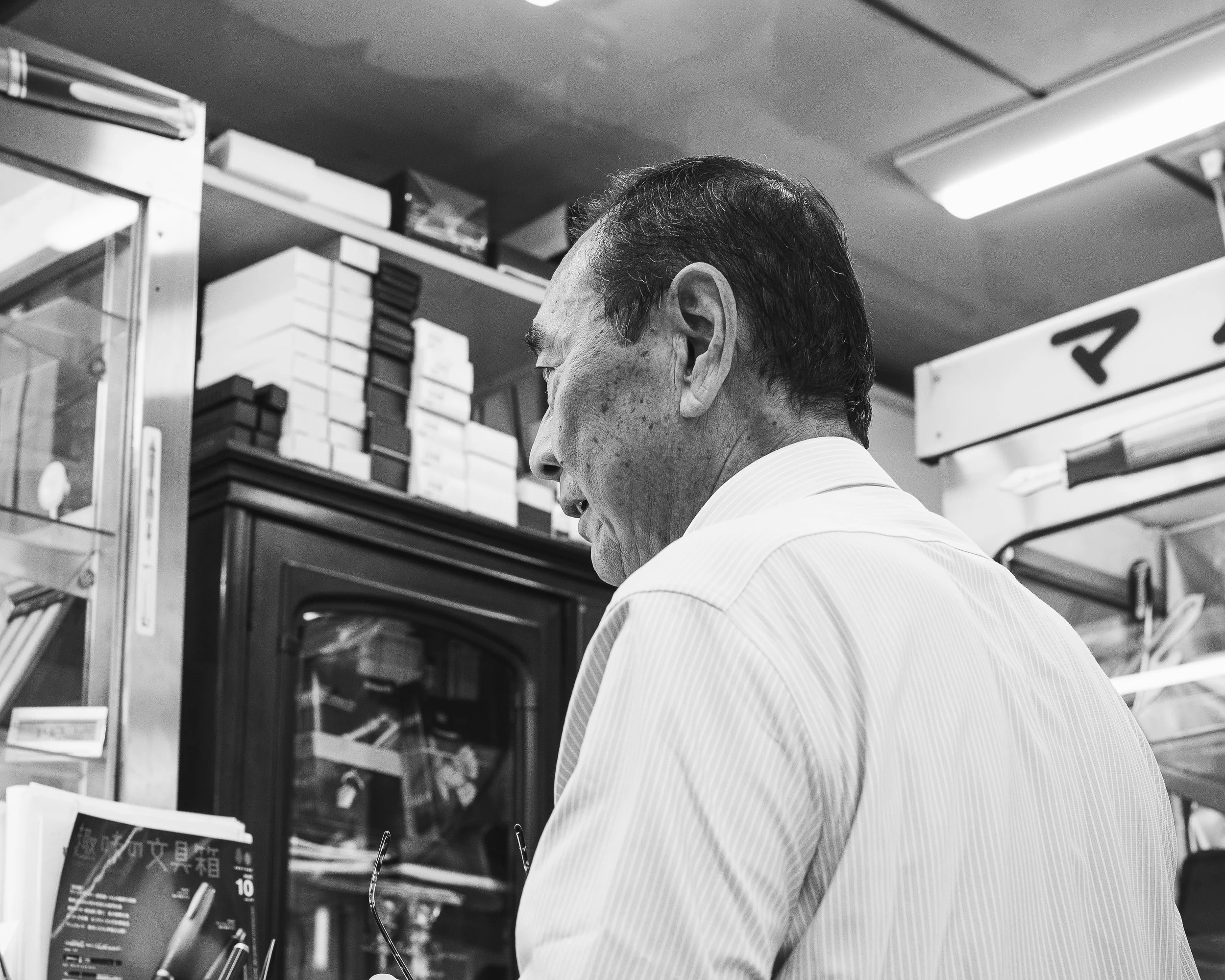 A man with glasses and a white shirt standing inside a shop, looking at items on a shelf.