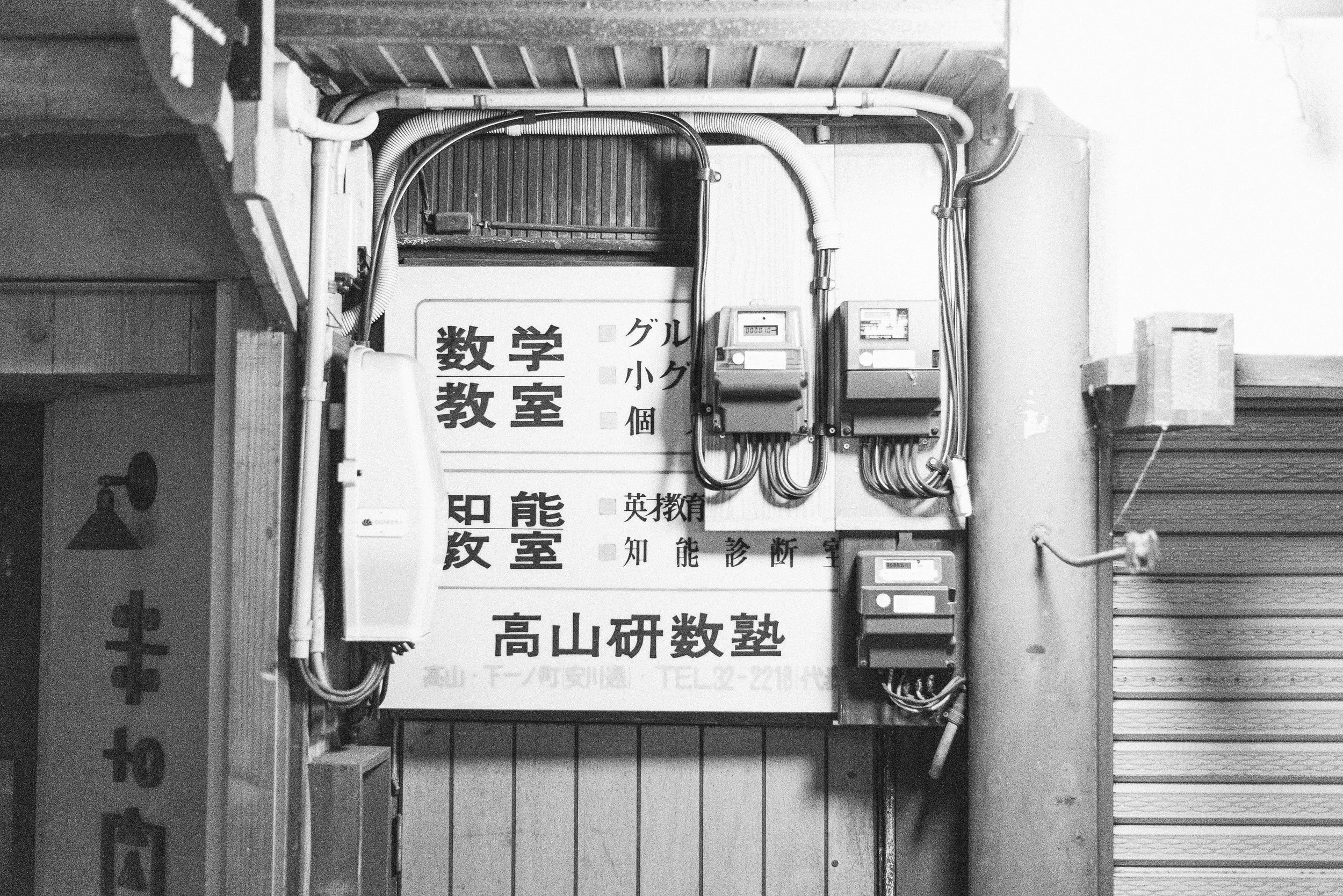 A black and white photo of an electrical panel and sign with Japanese text.
