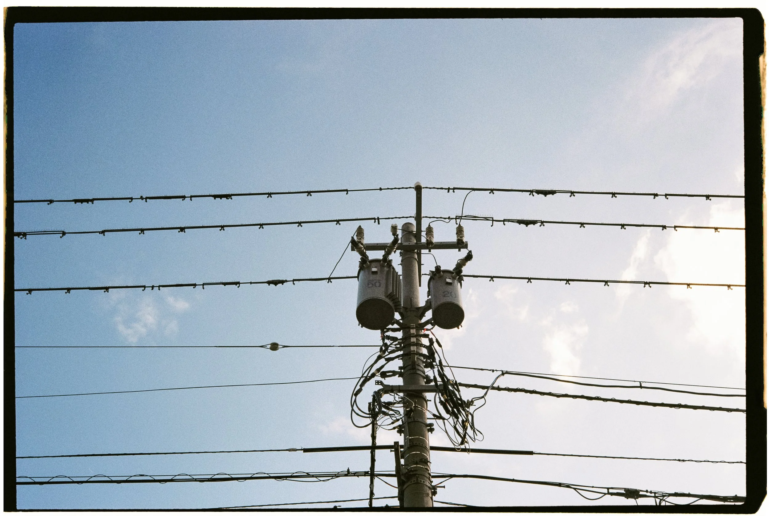 View of electrical power lines and transformers on a utility pole against a partly cloudy blue sky.